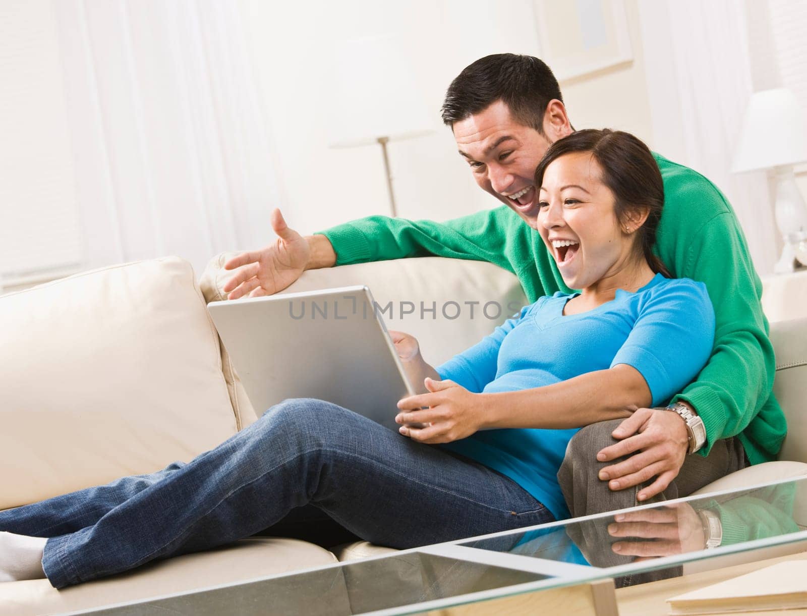 An attractive young couple sitting on a couch together and viewing laptop screen. They are laughing. Horizontally framed shot.