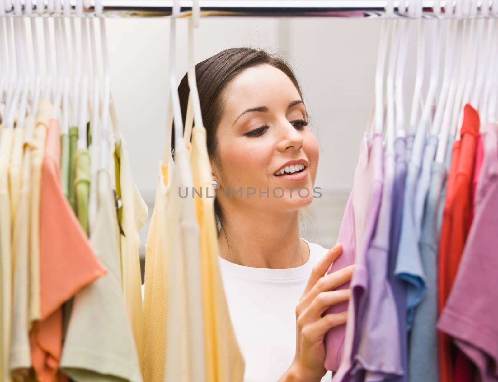 An attractive young female looking through a clothing closet. She is smiling. Horizontally framed photo.