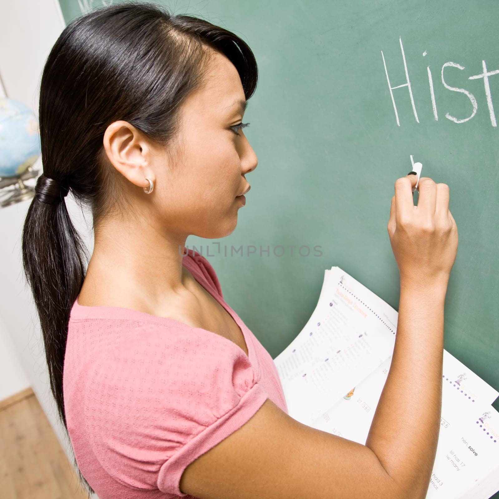 Teacher writing on chalk board in classroom. Square format.