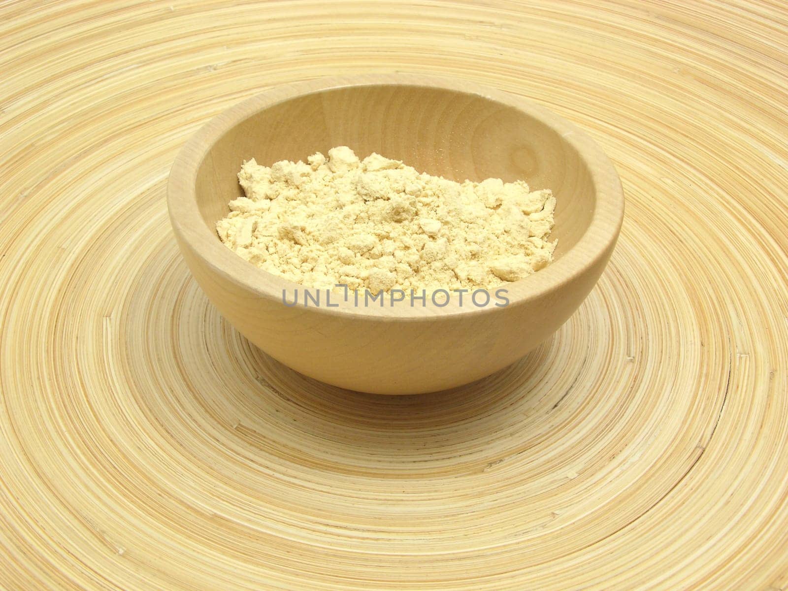 Wooden bowl with soy flour on bamboo plate