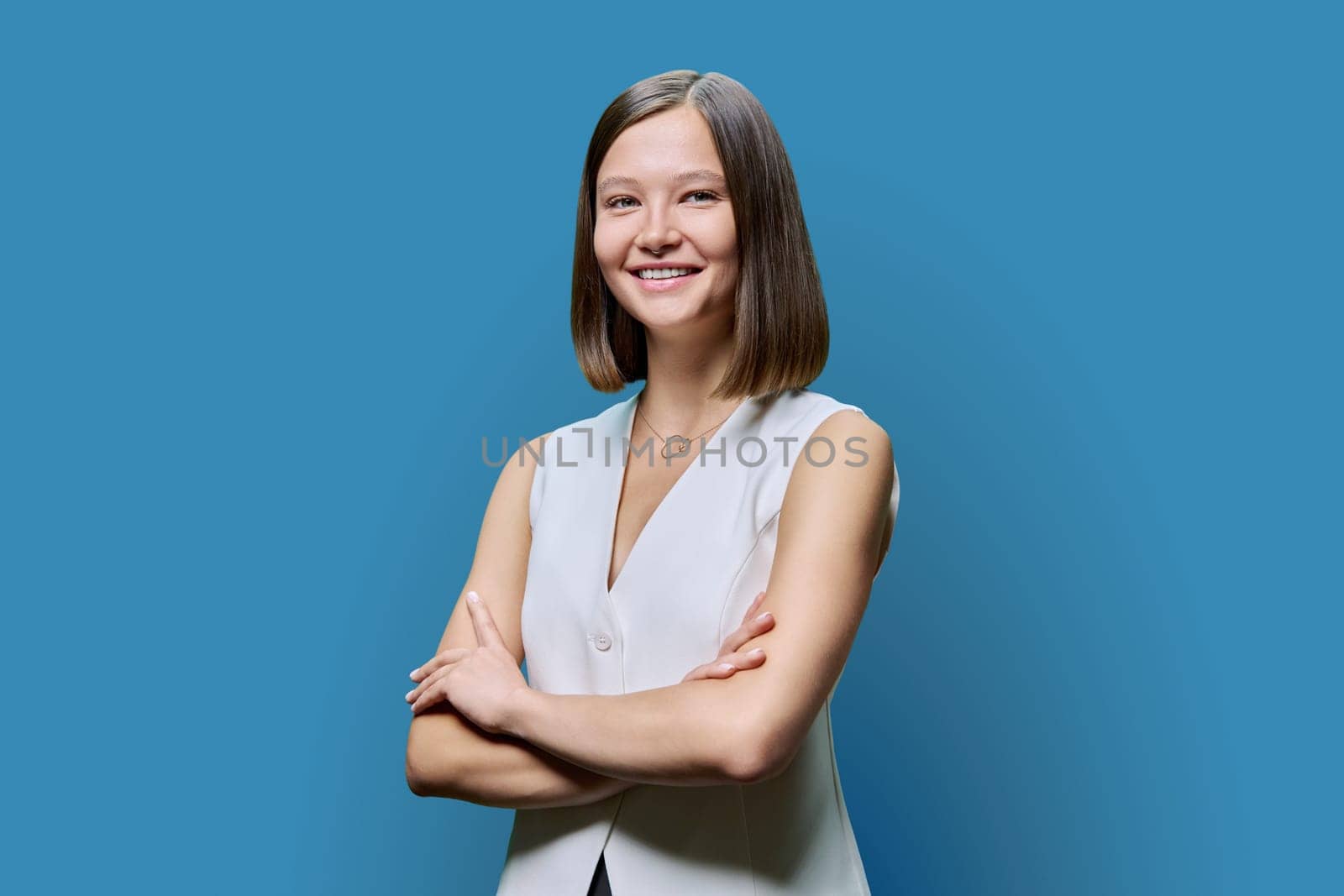 Portrait of young confident woman on blue studio background. Successful fashionable female with crossed arms looking at camera. Business, work, services, education, fashion beauty professions