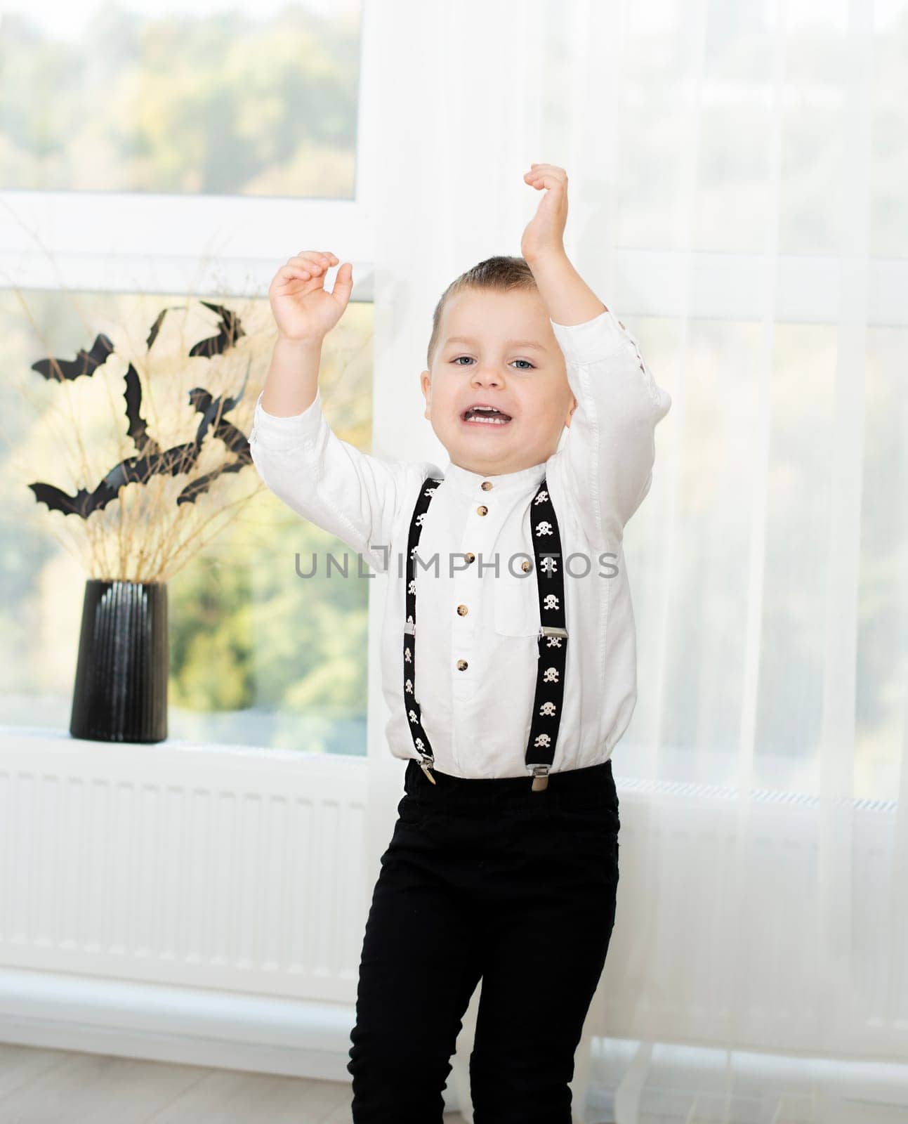 Halloween concept. Autumn holiday. A boy dances against the background of a window near a black vase with bats cut out of paper on dry branches. Close-up. Background.