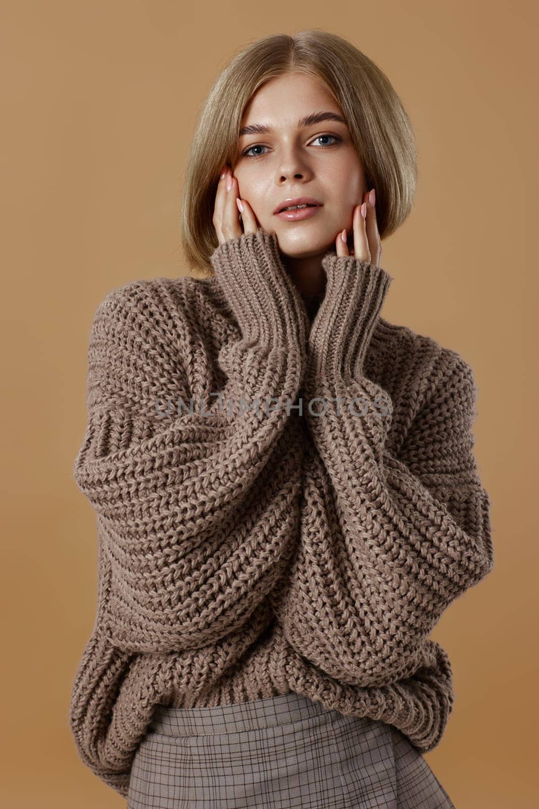 beautiful blonde woman in brown knitted sweater on beige background. autumn style