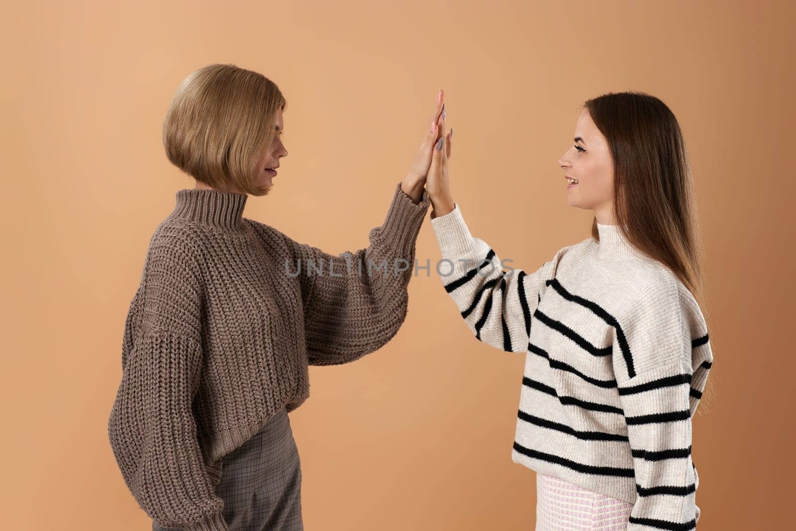 two young women friends giving high five hold hands on beige background