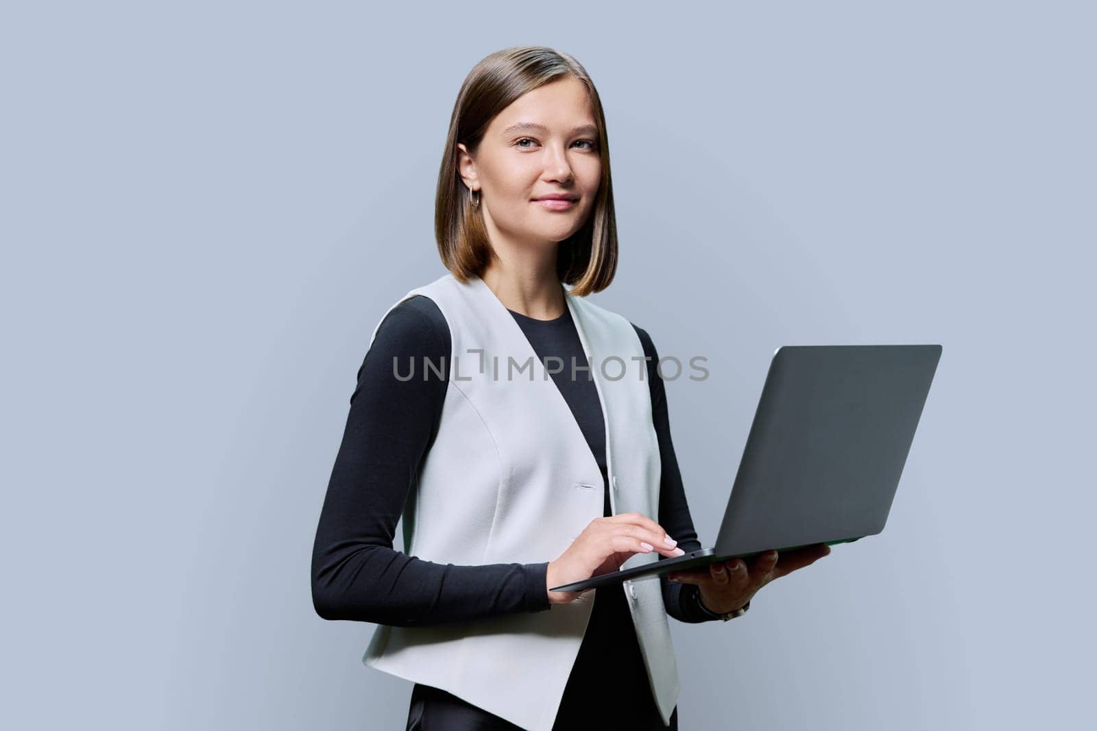 Smiling young business woman with laptop on grey studio background. Successful confident caucasian female looking at camera. Business, work, job, study, education, e-learning, technology concept