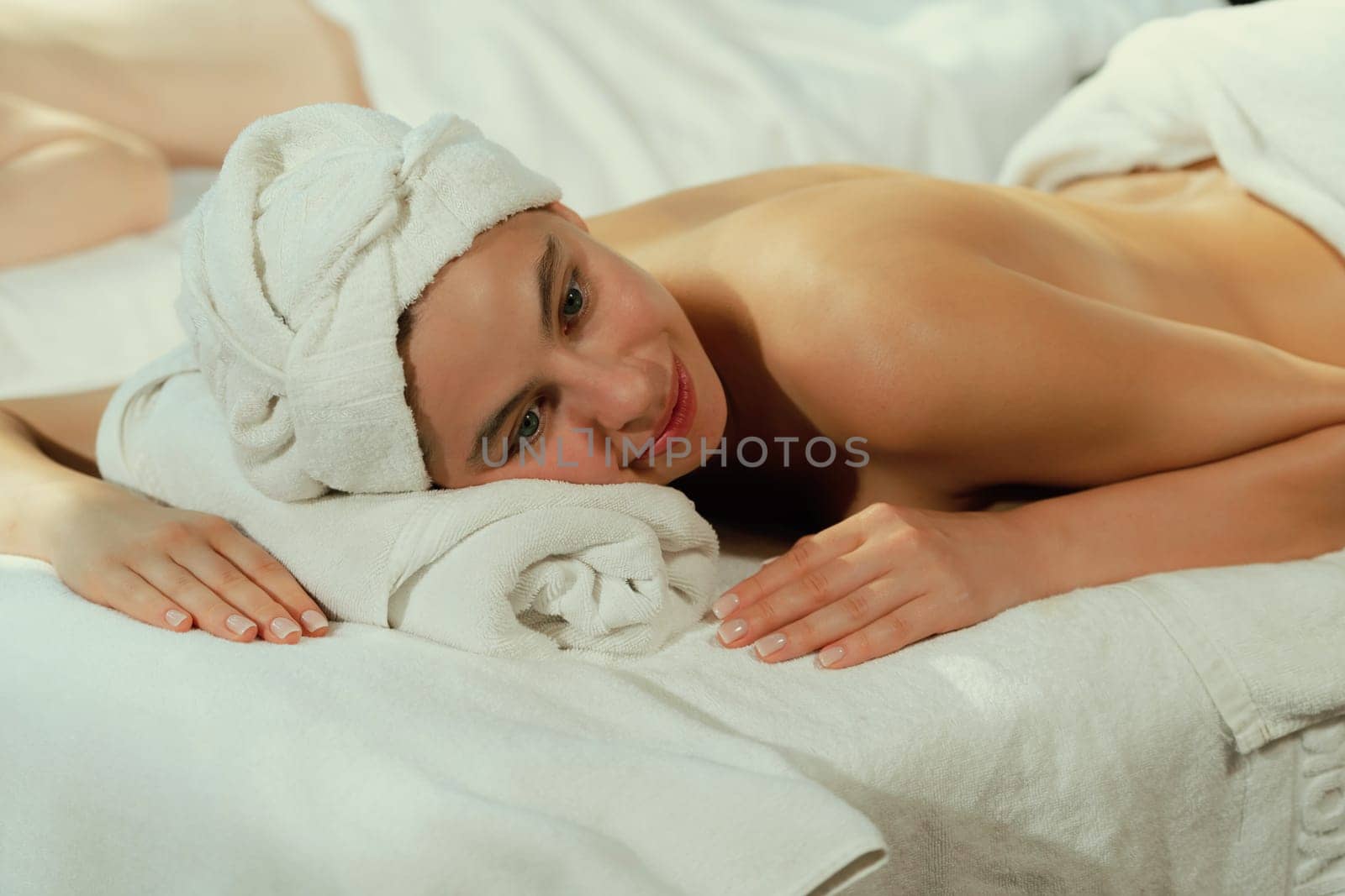 Beautiful young woman lies on a spa bed waiting for body massage. Relaxed and at peace concept. Pretty caucasian girl surrounded by gentle aroma of essential oils at spa salon. Close up. Tranquility.