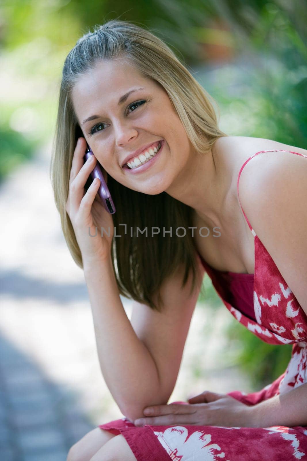 Smiling young woman talking on a cell phone in an outdoor setting. Vertical format.
