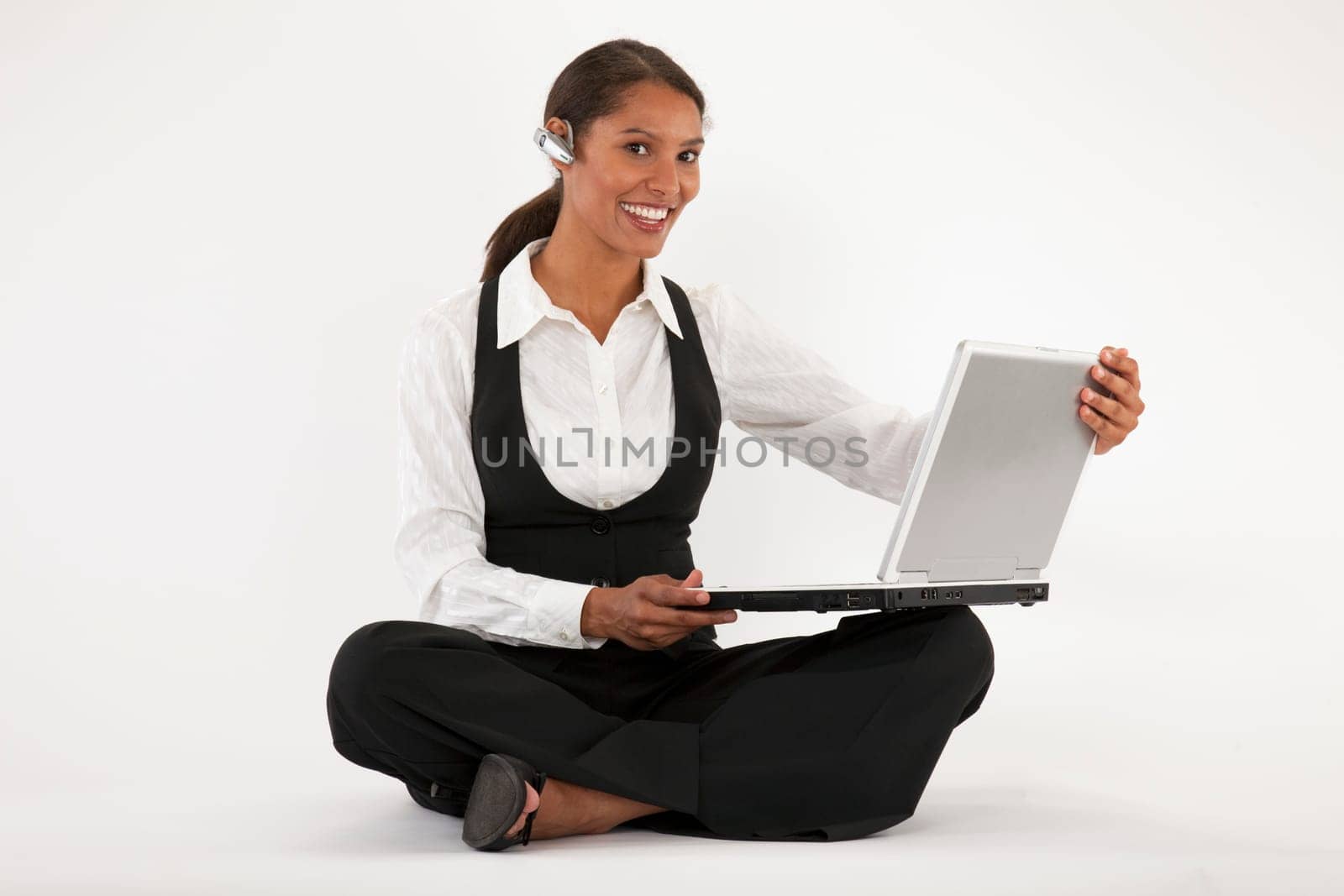 Young woman sitting on floor using laptop and wearing blue tooth headset. Horizontally format.
