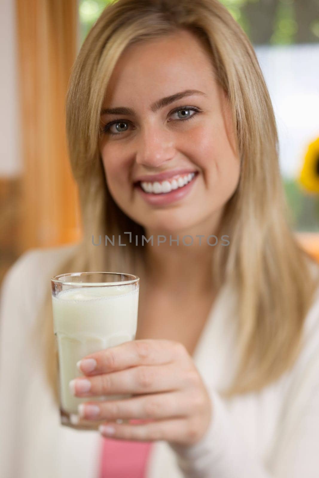 A young woman is holding a glass of milk and smiling at the camera.  Vertically framed shot.