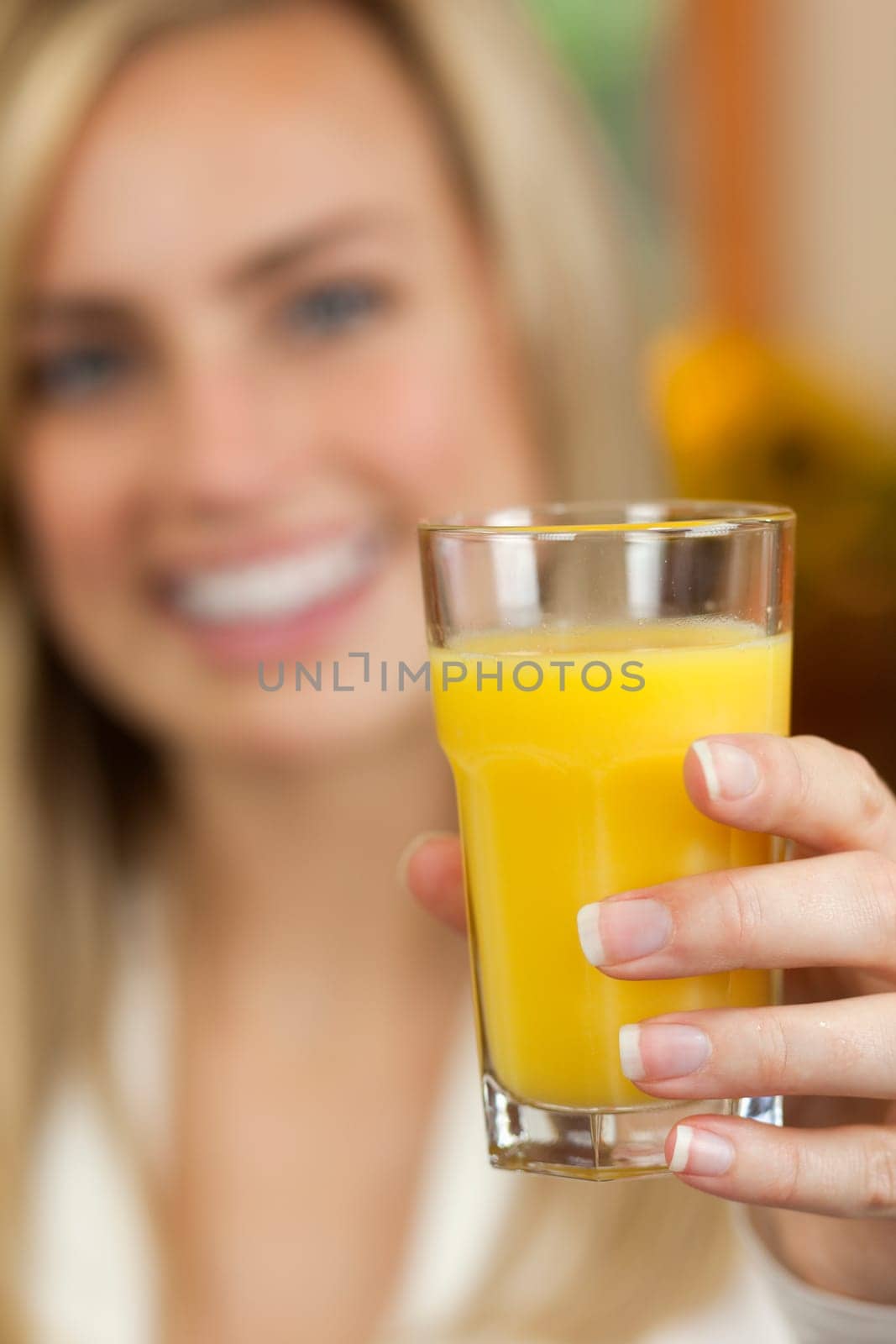 A young woman is holding a glass of orange juice and smiling at the camera.  Vertically framed shot.