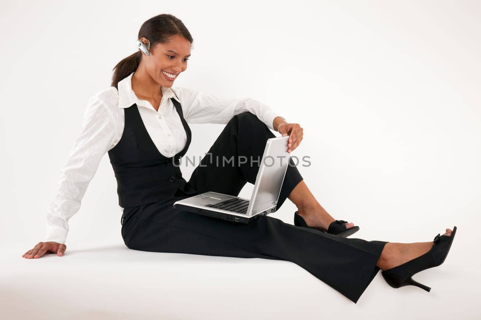 Young woman sitting on floor using laptop and wearing blue tooth headset. Horizontally format.