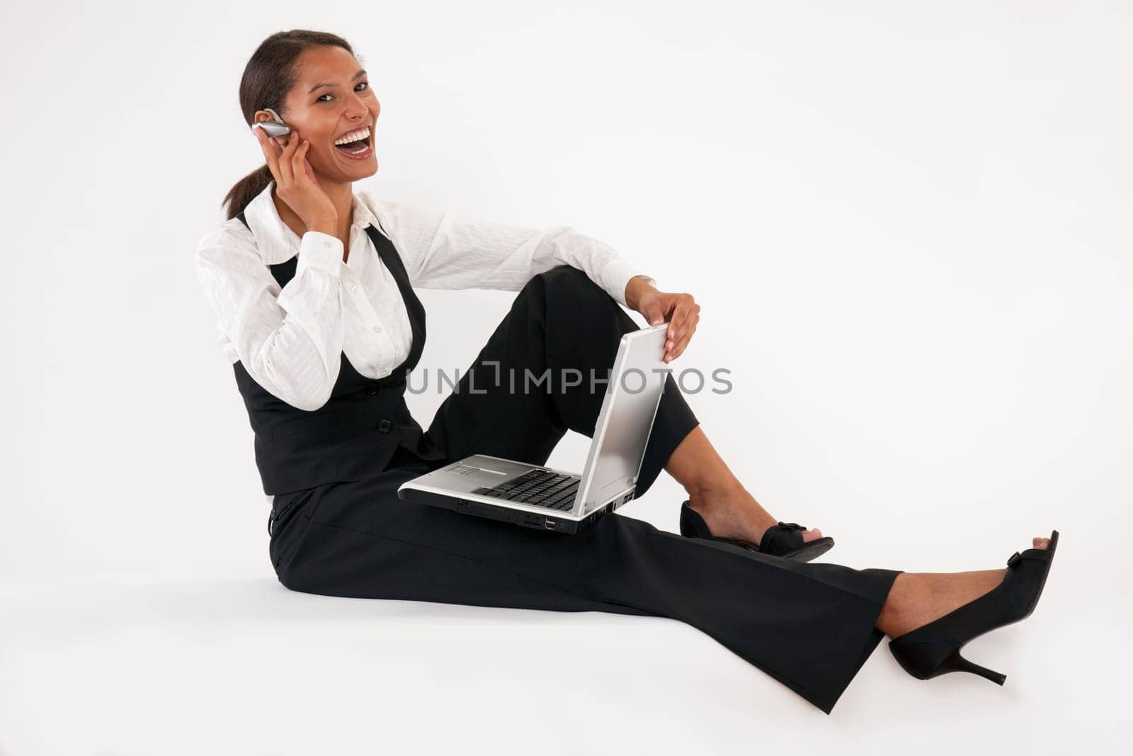 Young woman sitting on floor using laptop and wearing bluetooth headset. Horizontally format.