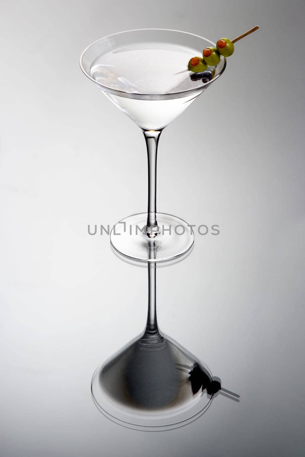 Martini mixed drink with olive garnish on a light grey background with reflection
