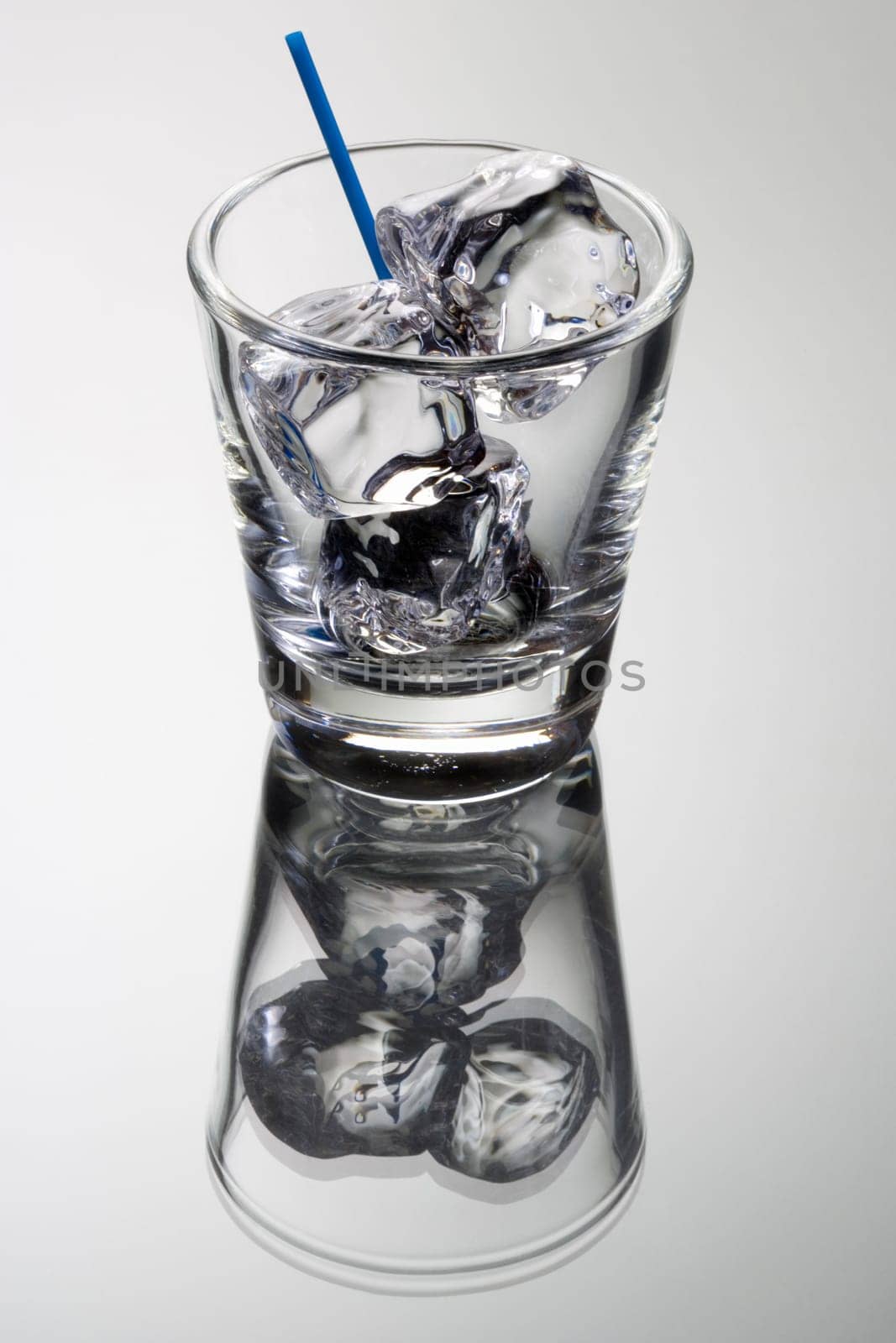 Empty mixed drink tumbler with ice on grey background with relfection