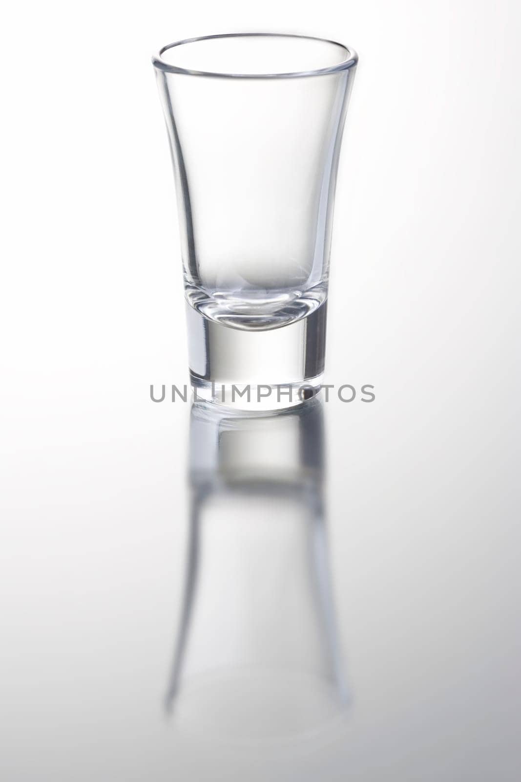 empty shot glass on grey background with reflection