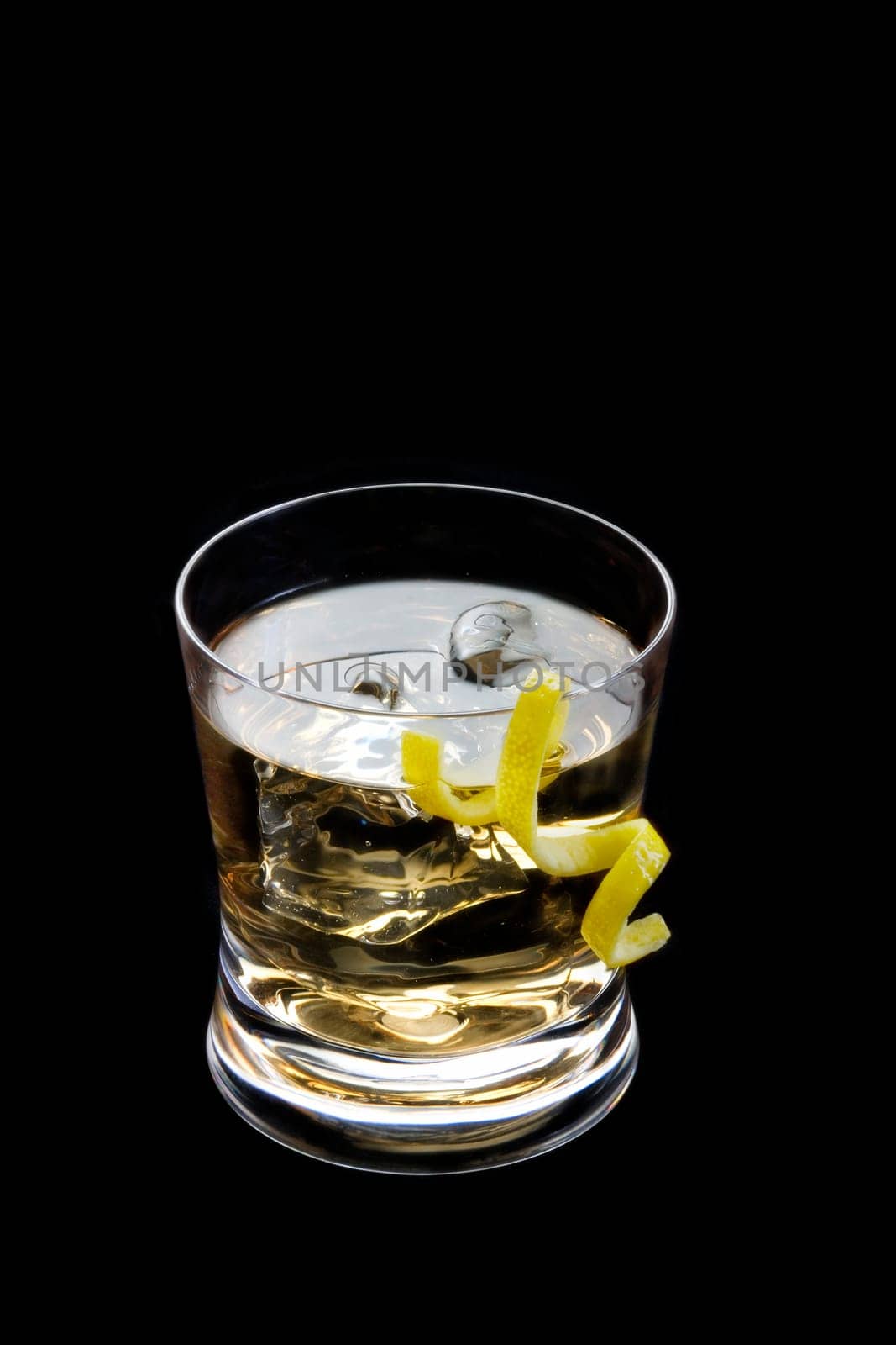 Rusty nail mixed drink with lemon peel on a black background