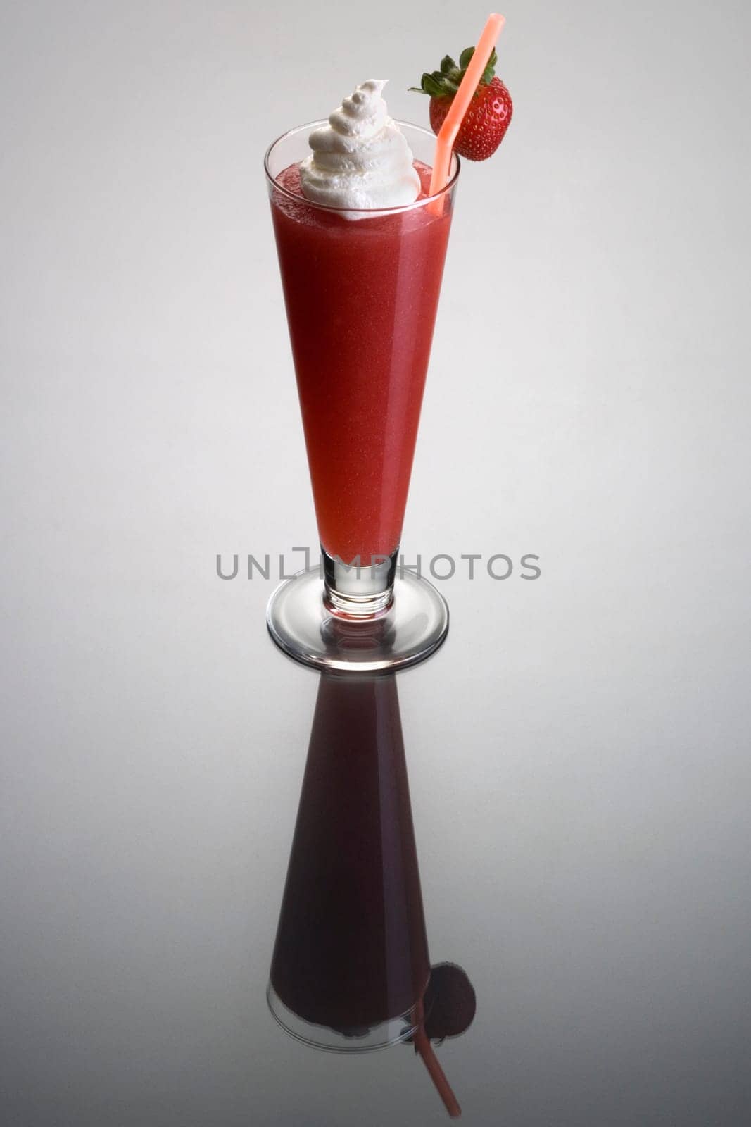 Frozen strawberry Daiguiri mixed drink with whipped cream and fruit garnish on plain background with eflection