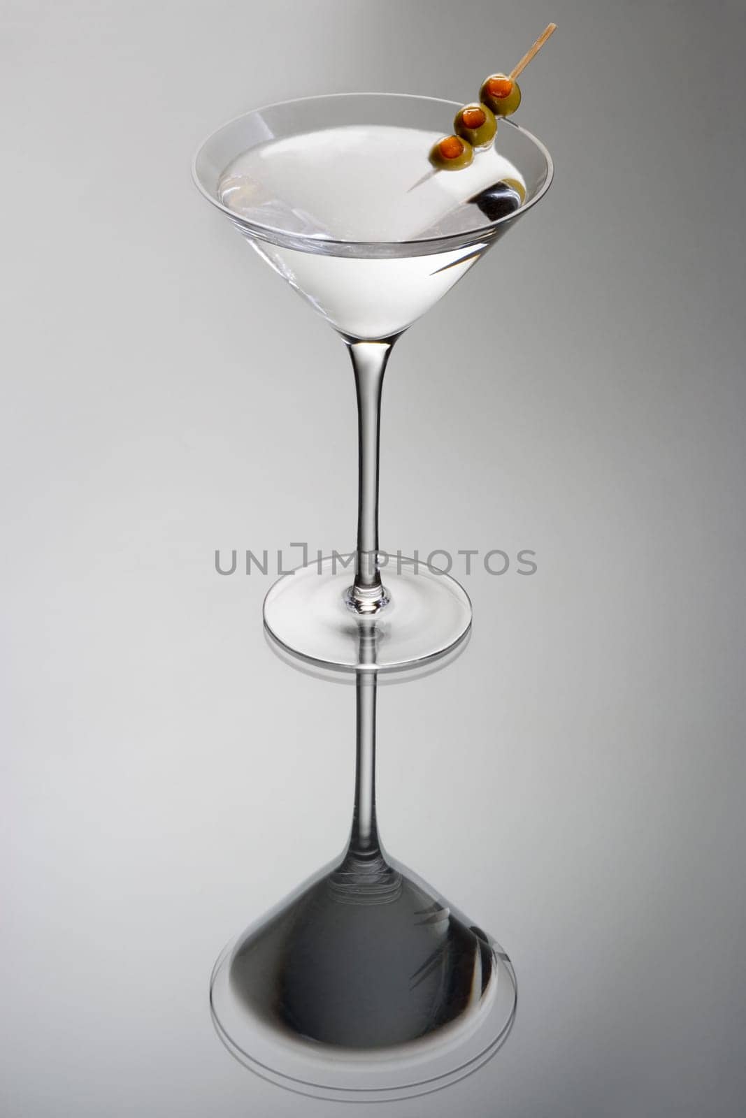 Martini mixed drink with olive garnish on a light grey background with reflection