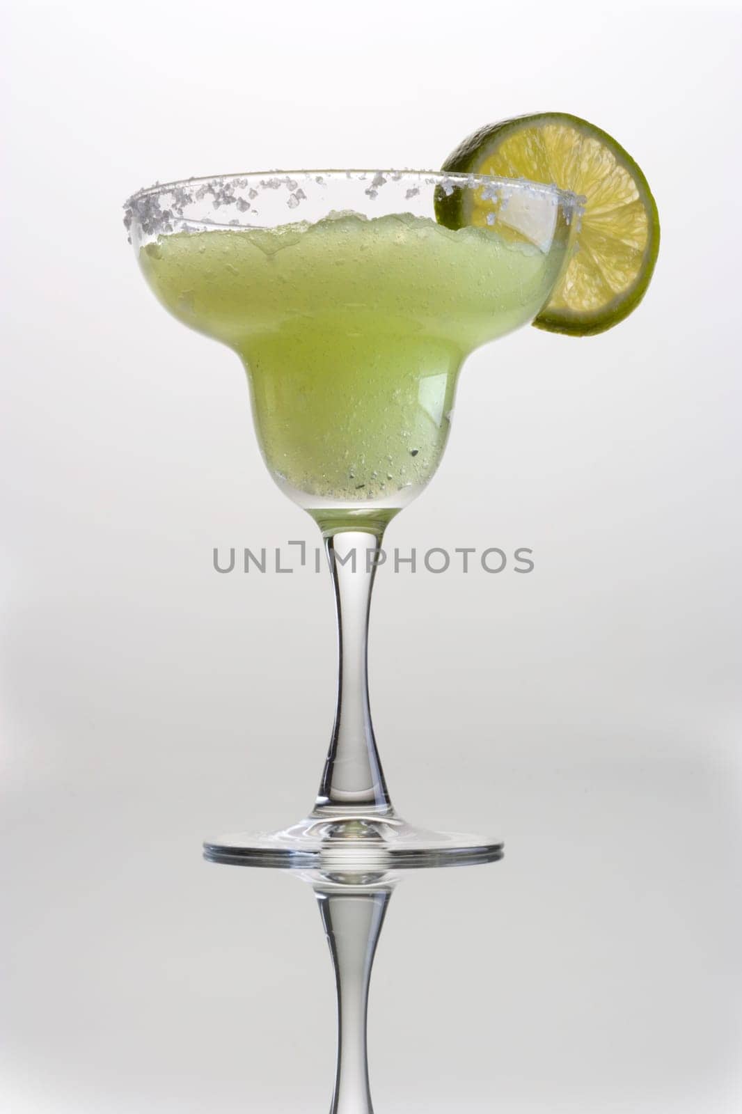Frozen Margarita mixed drink with lime slice garnish on plain grey background with reflection