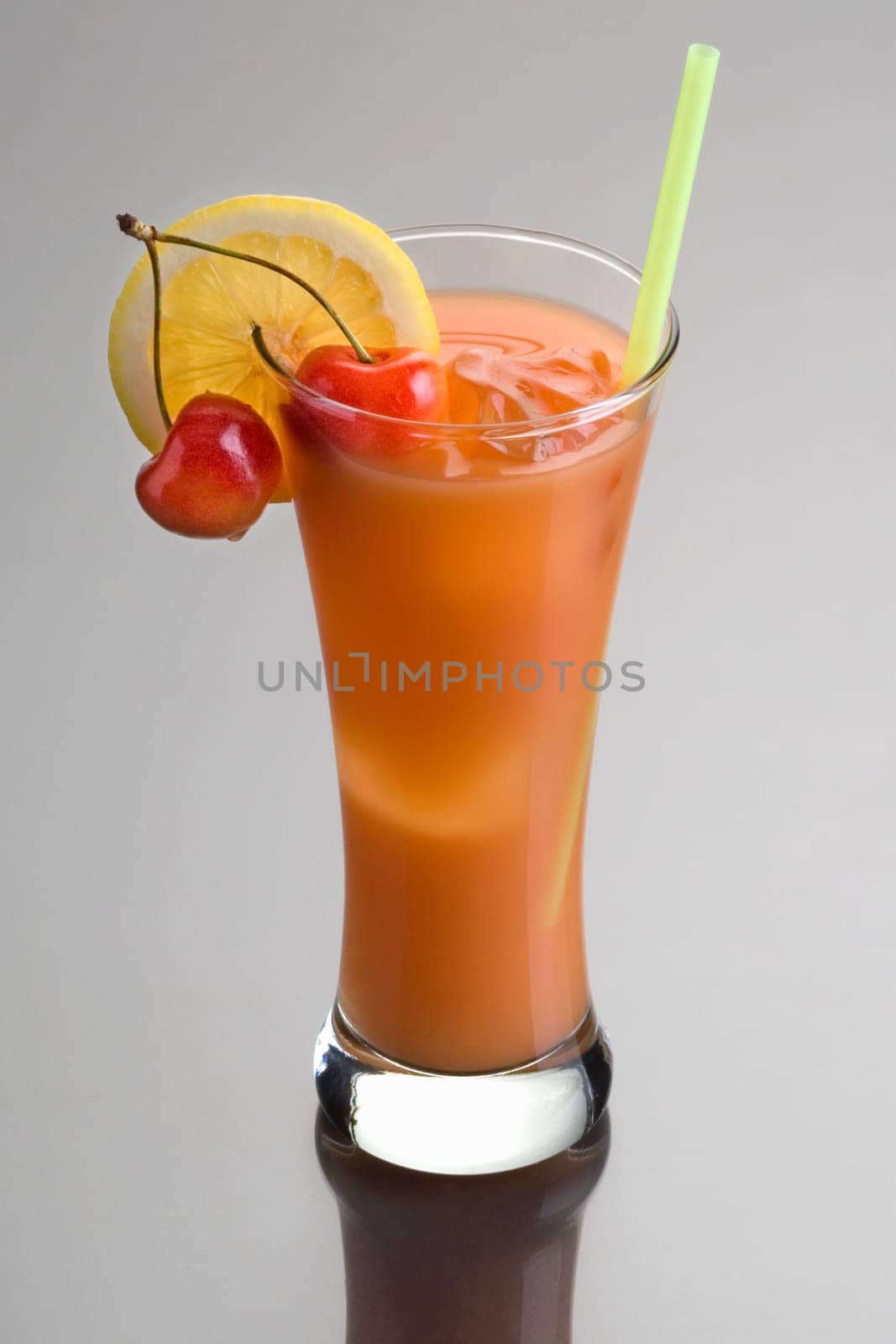 Zombie mixed drink with cherry and lemon garnish on grey background with reflection