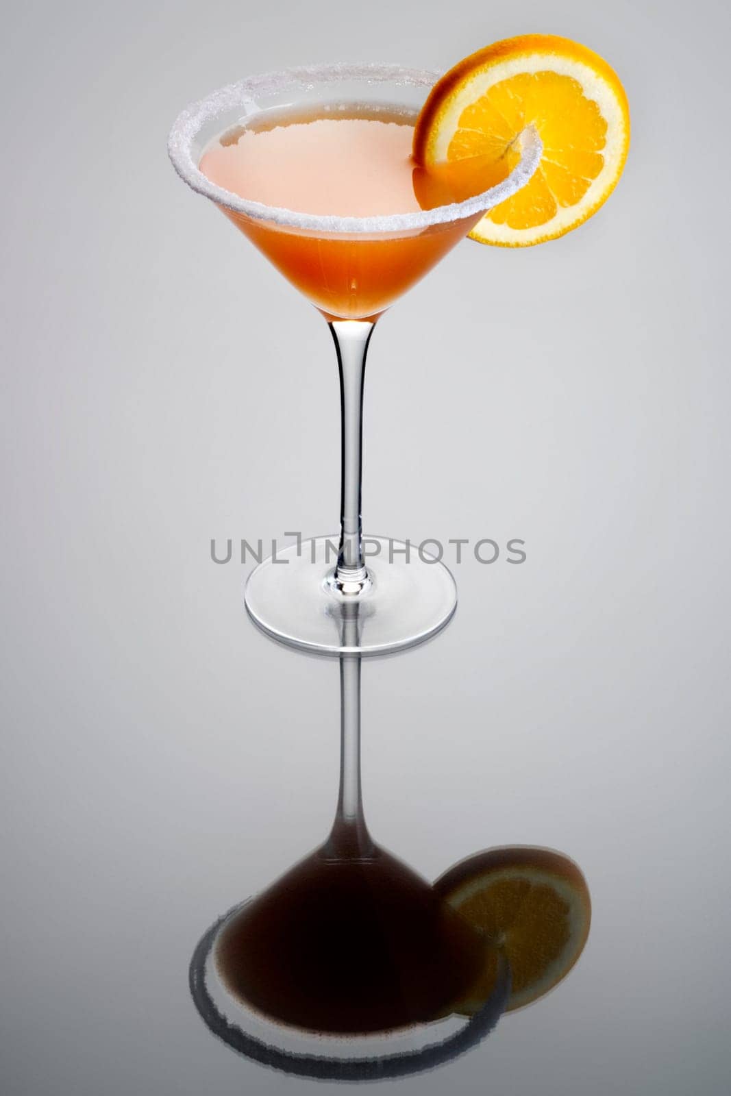 Sidecar mixed drink with orange garnish and sugar rim on plain grey background