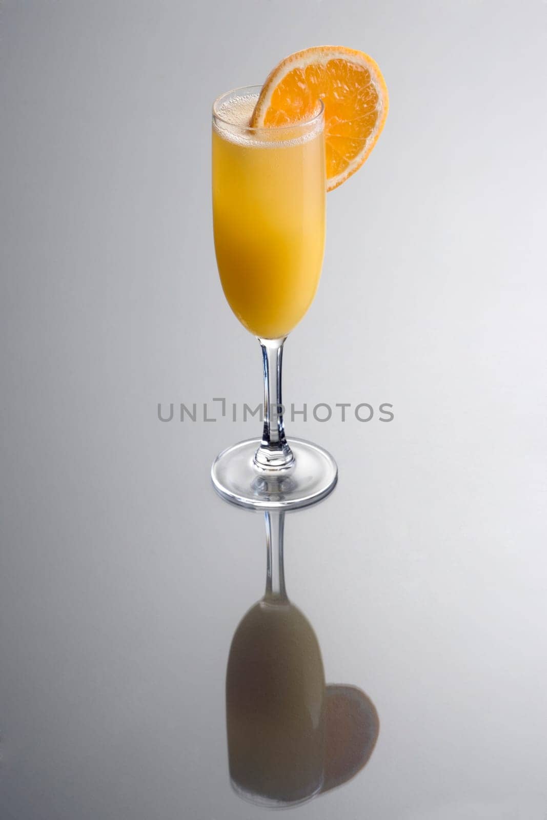 Mimosa mixed drink with orange slice garnish on grey background with reflection