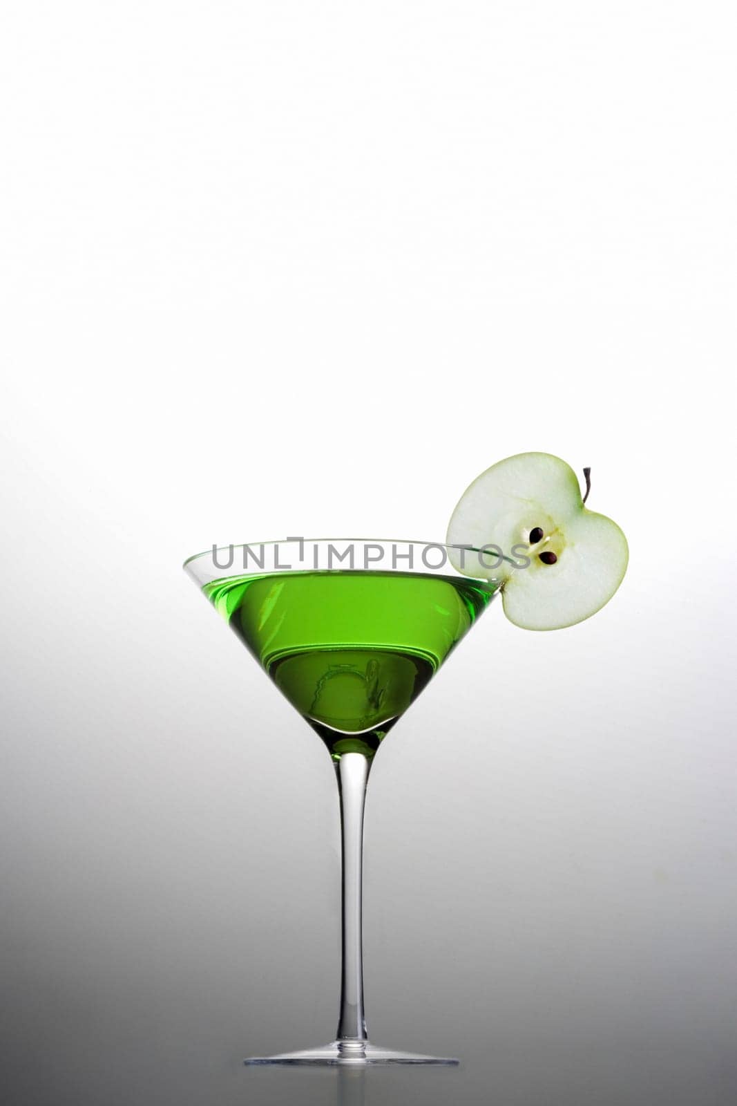 Apple Martini mixed drink with apple slice garnish on grey background