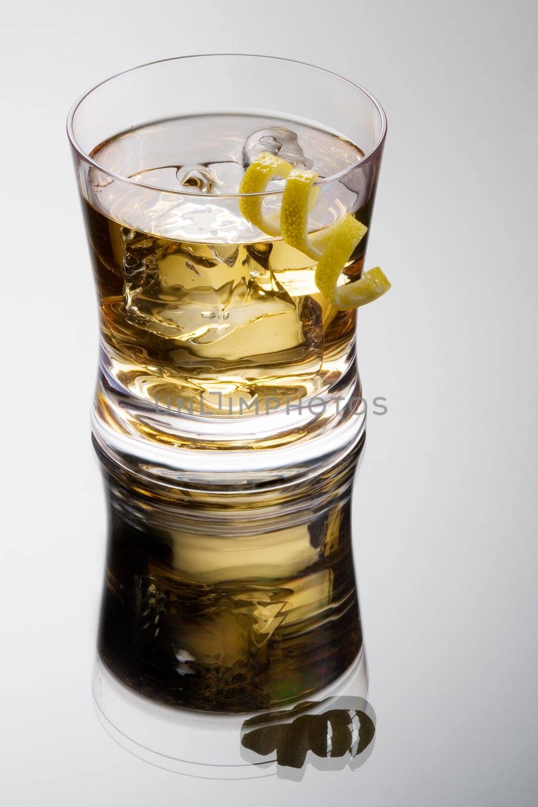 Rusty nail mixed drink with lemon peel on a grey background with reflection