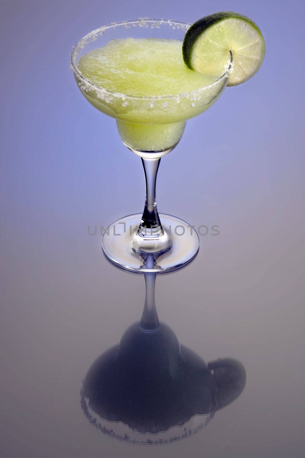 Frozen Margarita mixed drink with lime slice garnish on plain background with reflection