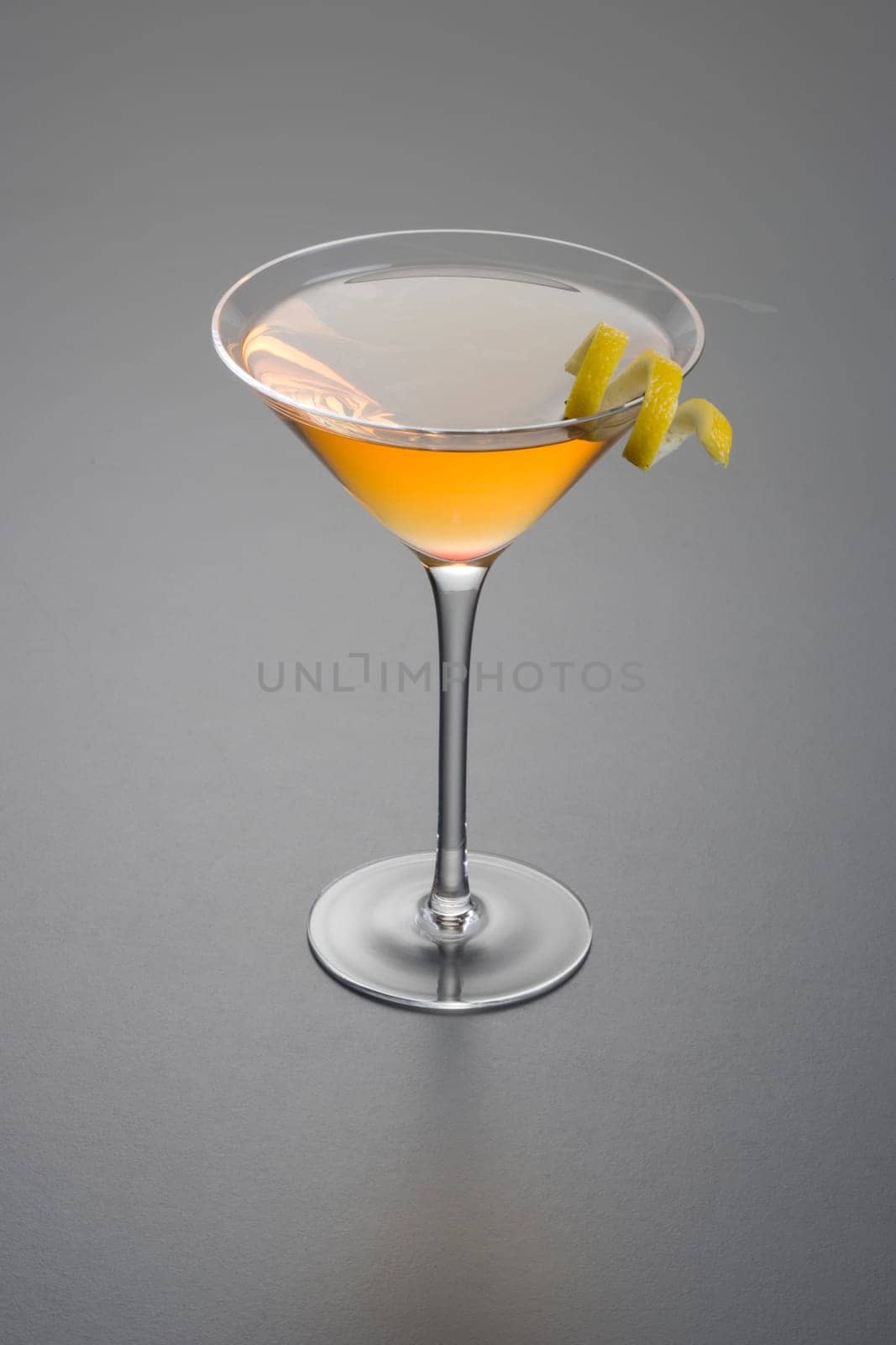 Manhattan cocktail with lemon peel garnish close up on grey background