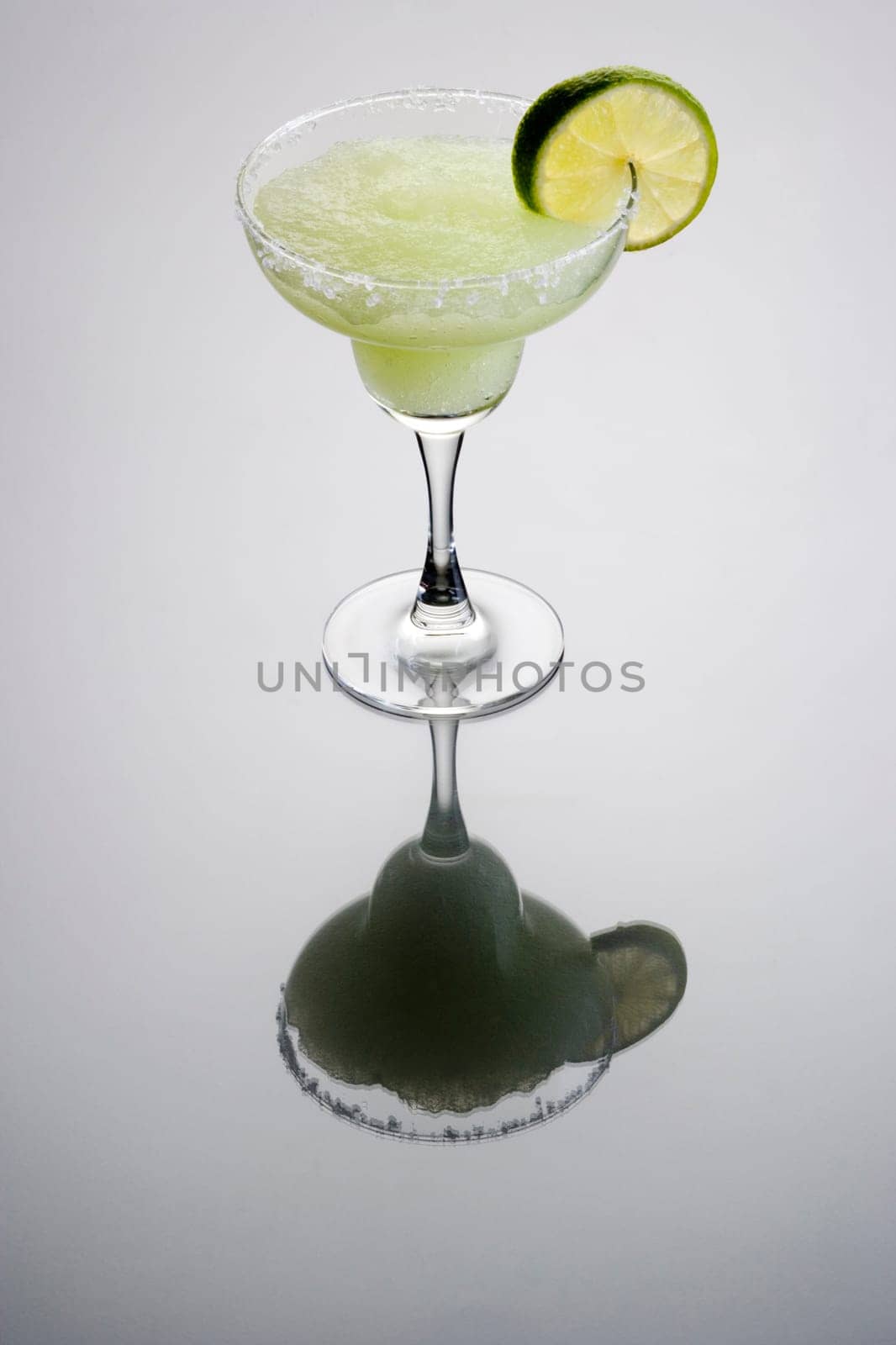 Frozen Margarita mixed drink with lime slice garnish on plain grey background with reflection