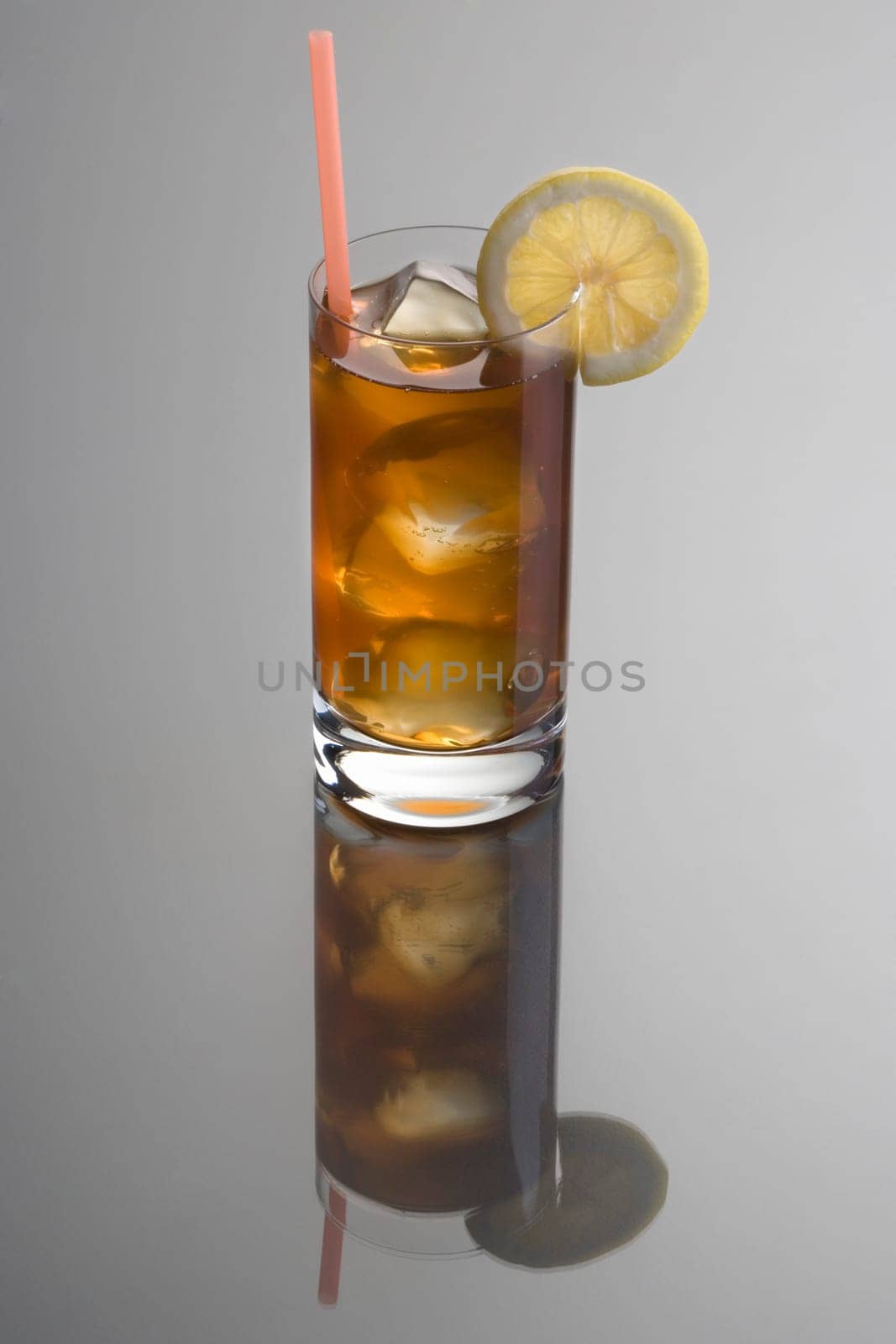 Long Island Ice Tea mixed drink with lemon slice garnish on grey background with reflection