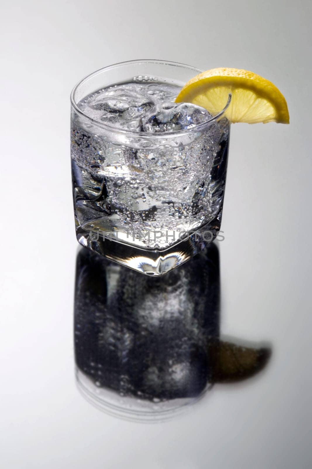 Club soda or Vodka / Gin and tonic mixed drink with lemon slice on a gray background with reflection