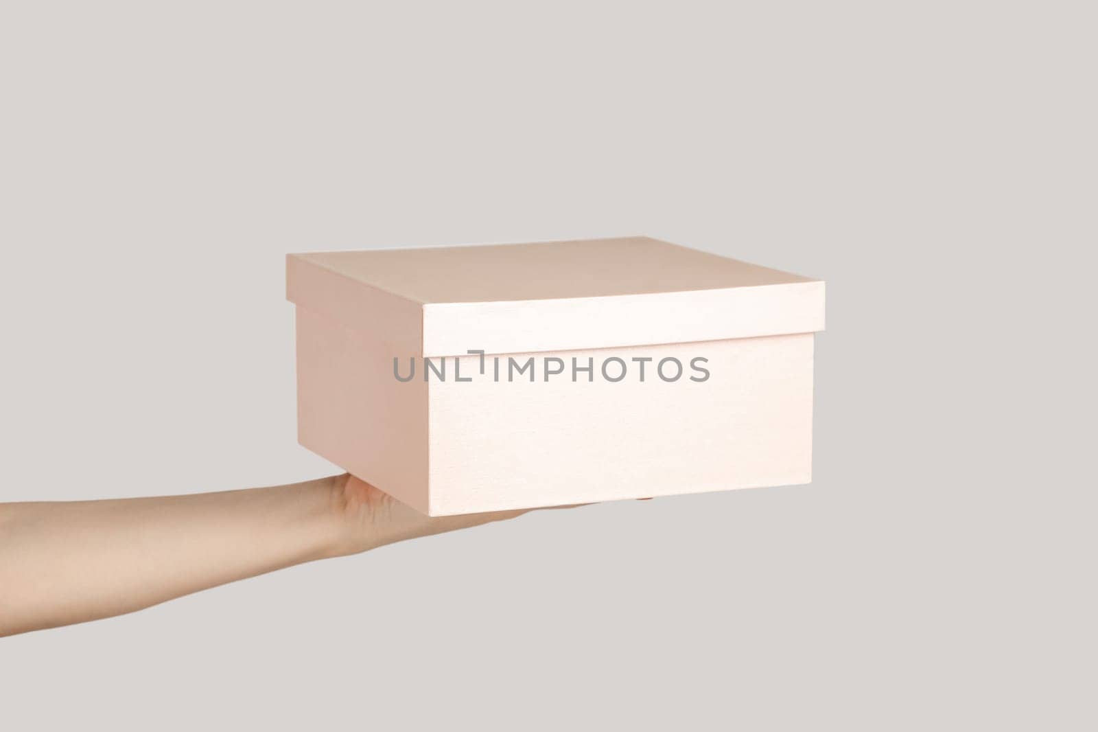 Closeup of woman hand showing present box, gift for holiday, event, celebration. Indoor studio shot isolated on gray background.