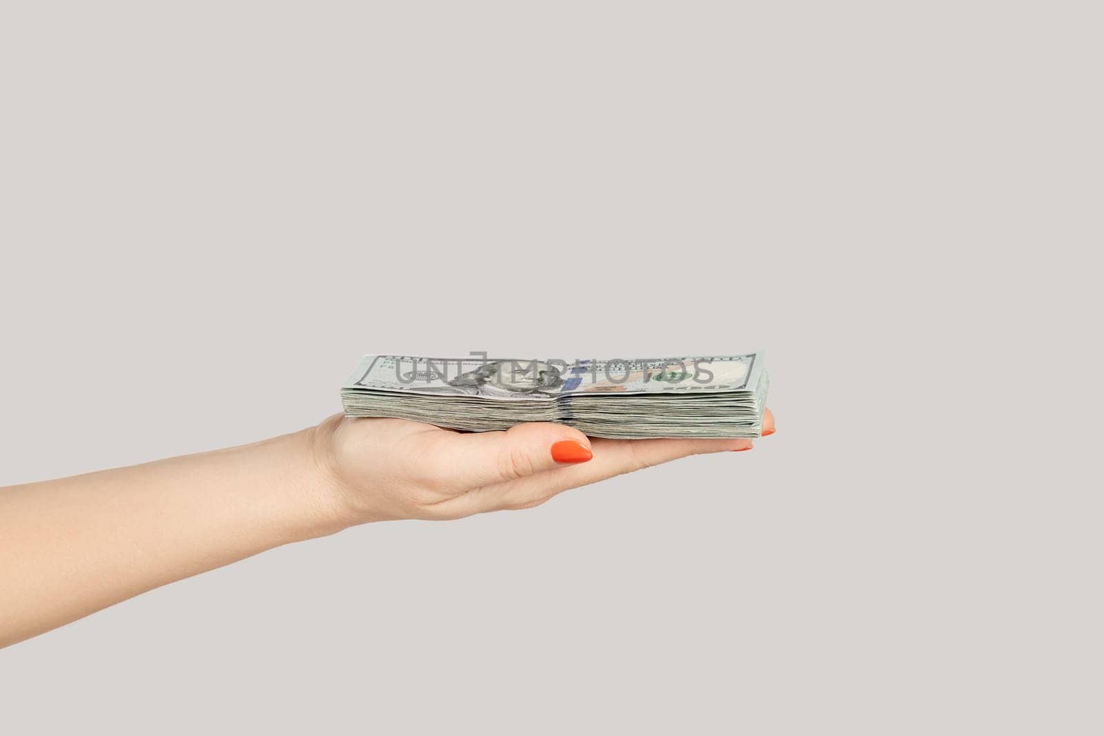 Closeup of woman hand showing dollar banknotes, earning money, salary, jackpot. Indoor studio shot isolated on gray background.