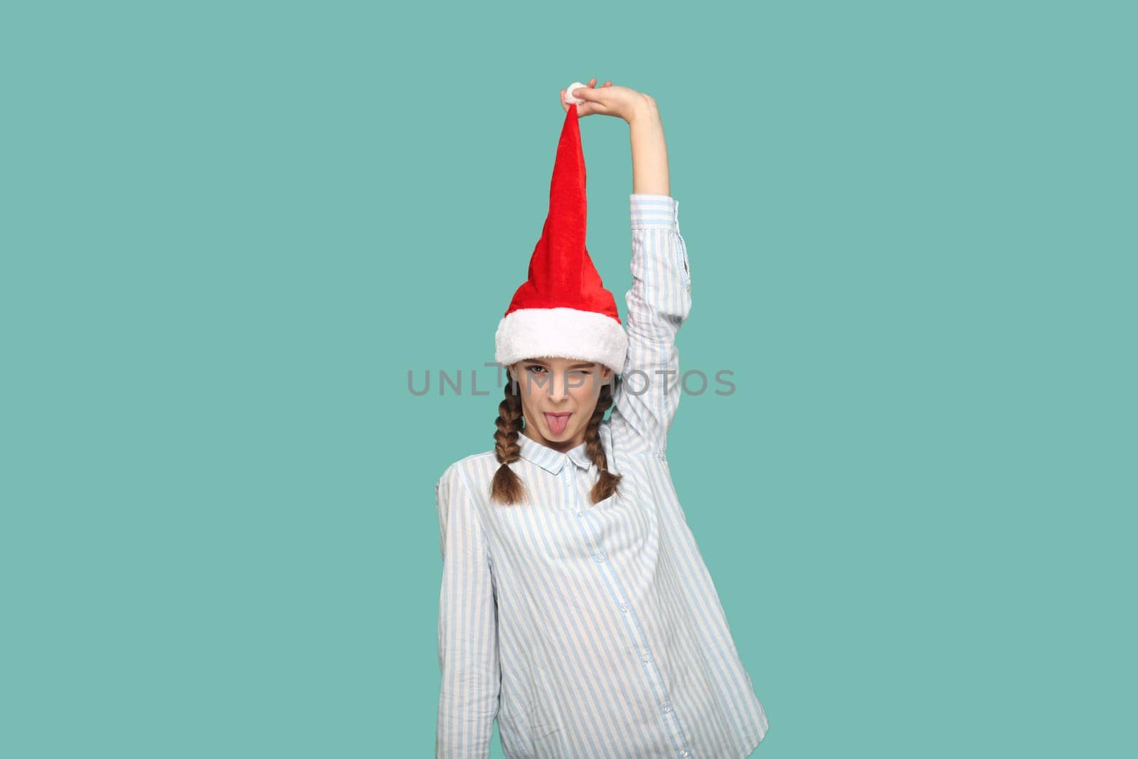 Happy funny teenager girl looking at camera with tongue out, pulling up her Santa Claus hat. by Khosro1