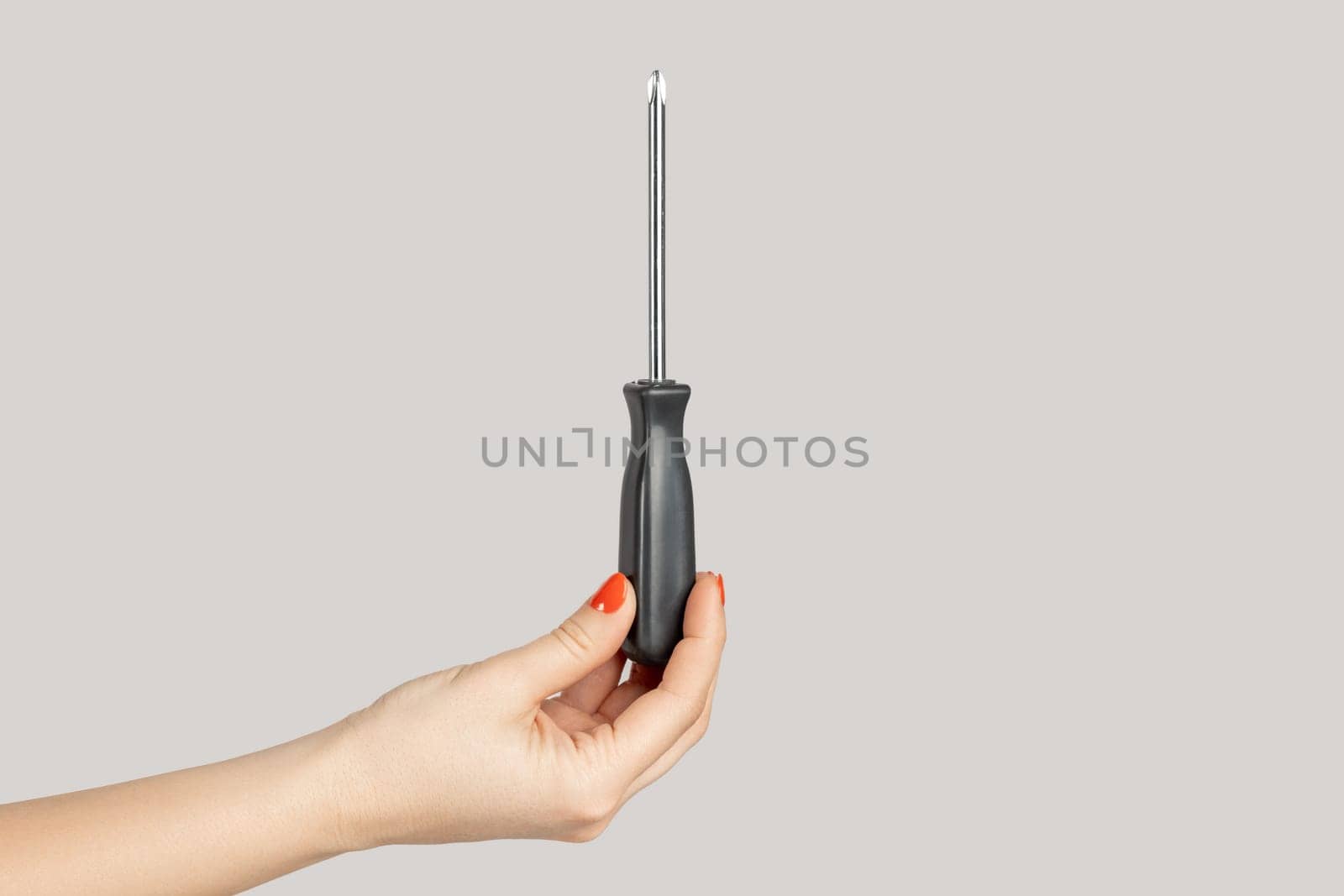 Closeup of woman hand showing black metal and plastic tool screwdriver for repair. Indoor studio shot isolated on gray background.