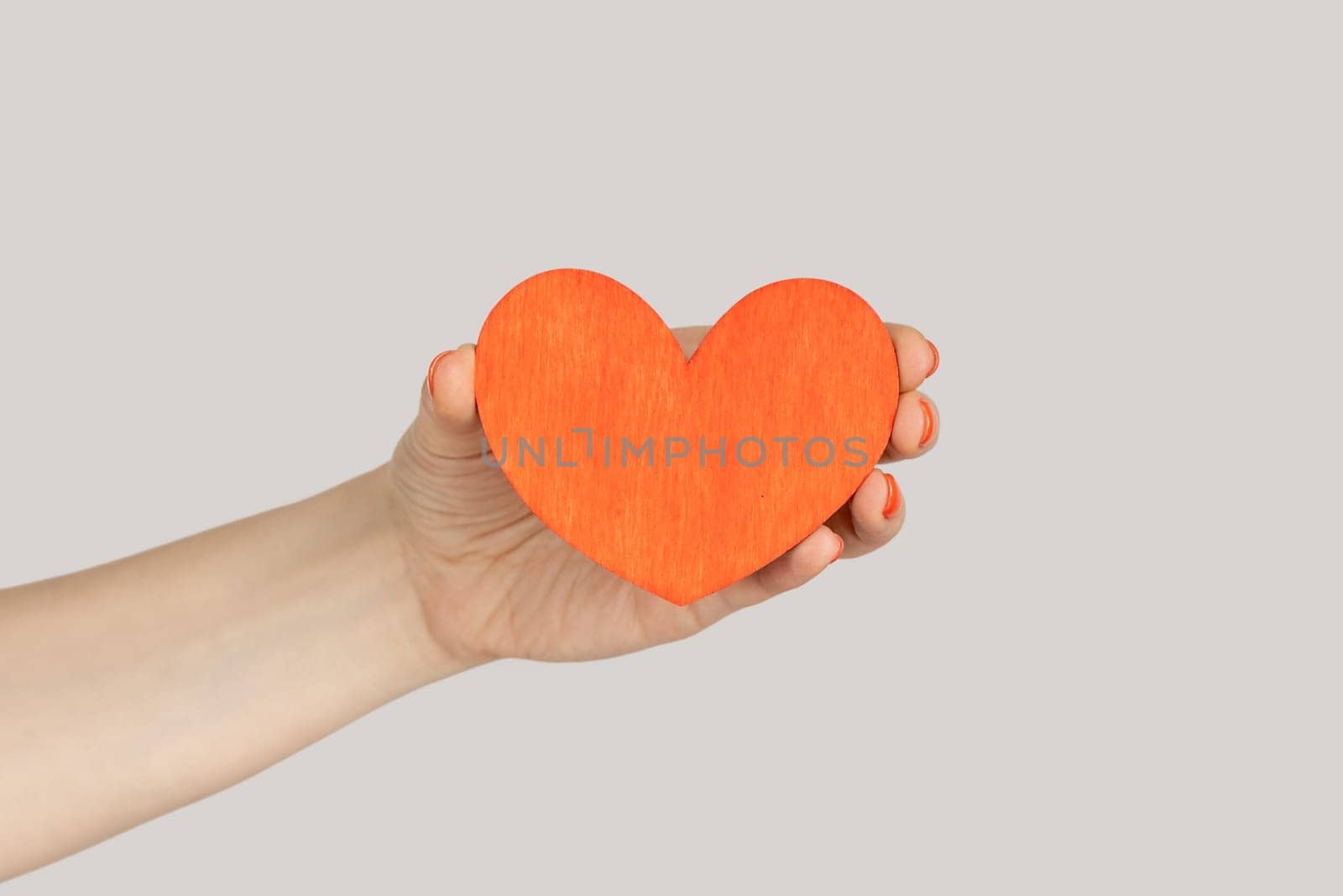 I love you. Closeup of woman hand showing little red paper heart symbol of love and devotion. Indoor studio shot isolated on gray background.