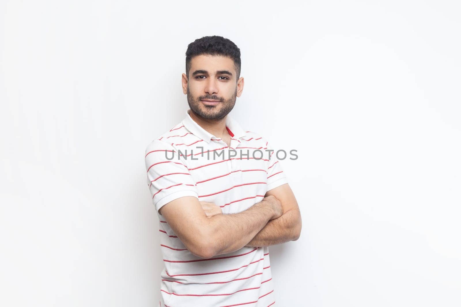 Delighted positive confident man wearing t-shirt standing with crossed hands, looking at camera. by Khosro1