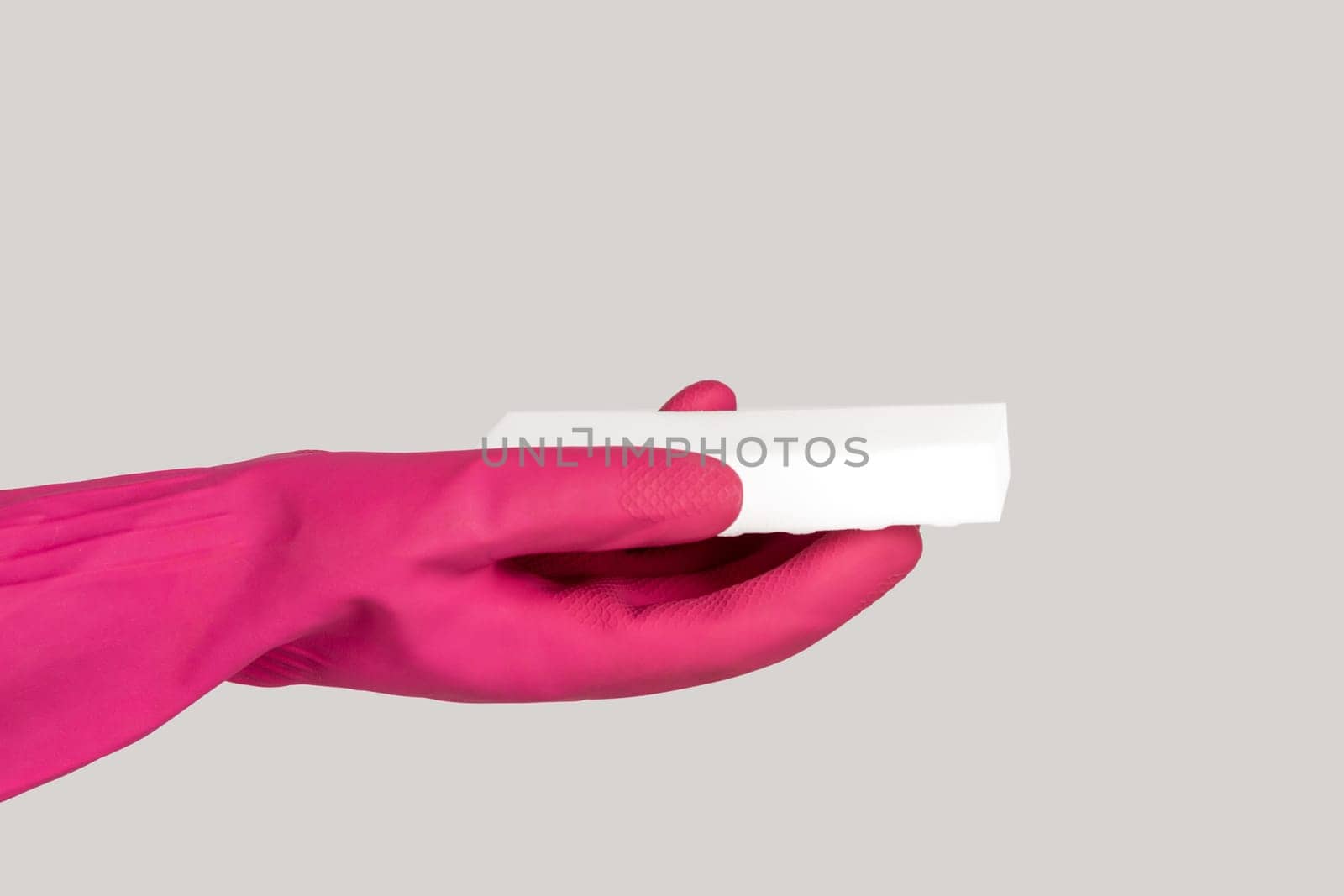 Closeup of woman hand in pink rubber glove holding dish washing white sponge cleaning service. Indoor studio shot isolated on gray background.