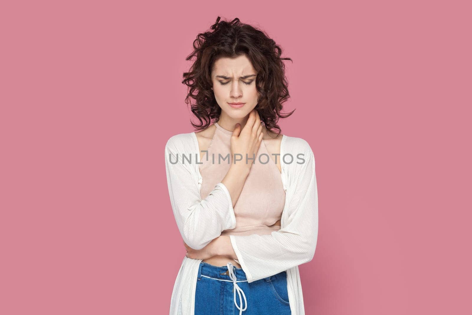 Portrait of sad upset unhappy woman with curly hair wearing casual style outfit standing looking down, crying, hearing bad news. Indoor studio shot isolated on pink background.