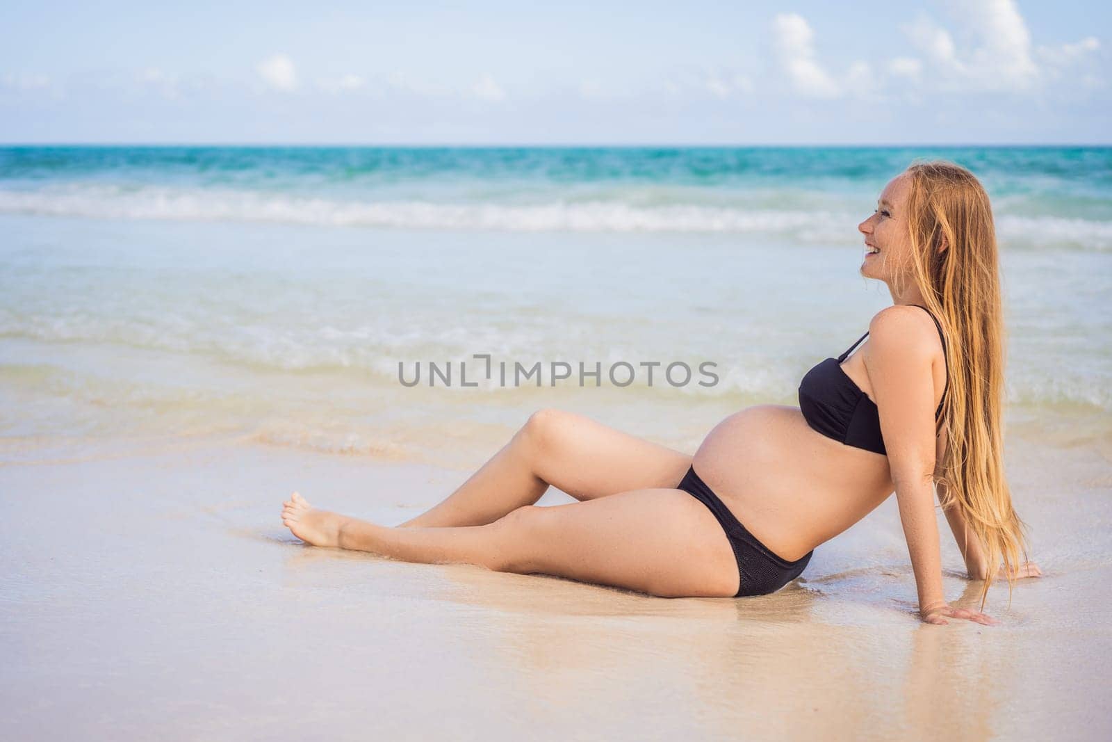 Radiant pregnant woman in a swimsuit, amid the stunning backdrop of a turquoise sea. Serene beauty of maternity by the shore.