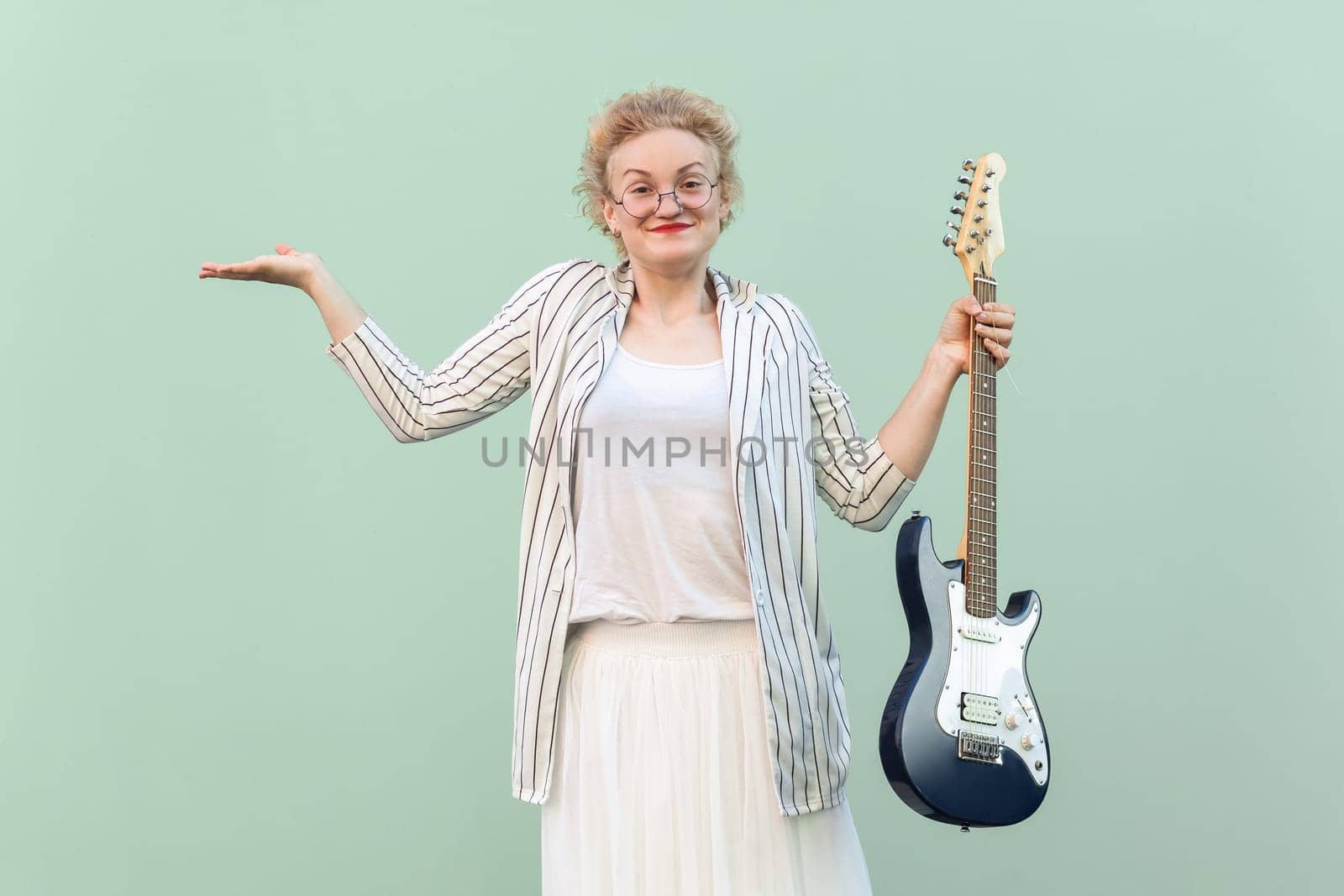 Uncertain woman with eyeglasses holding electric guitar, spreads hand, looks confused. by Khosro1