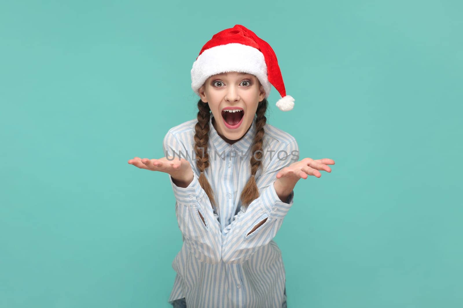 Excited amazed girl in Santa Claus hat, looking at camera with open mouth, spread hands. by Khosro1