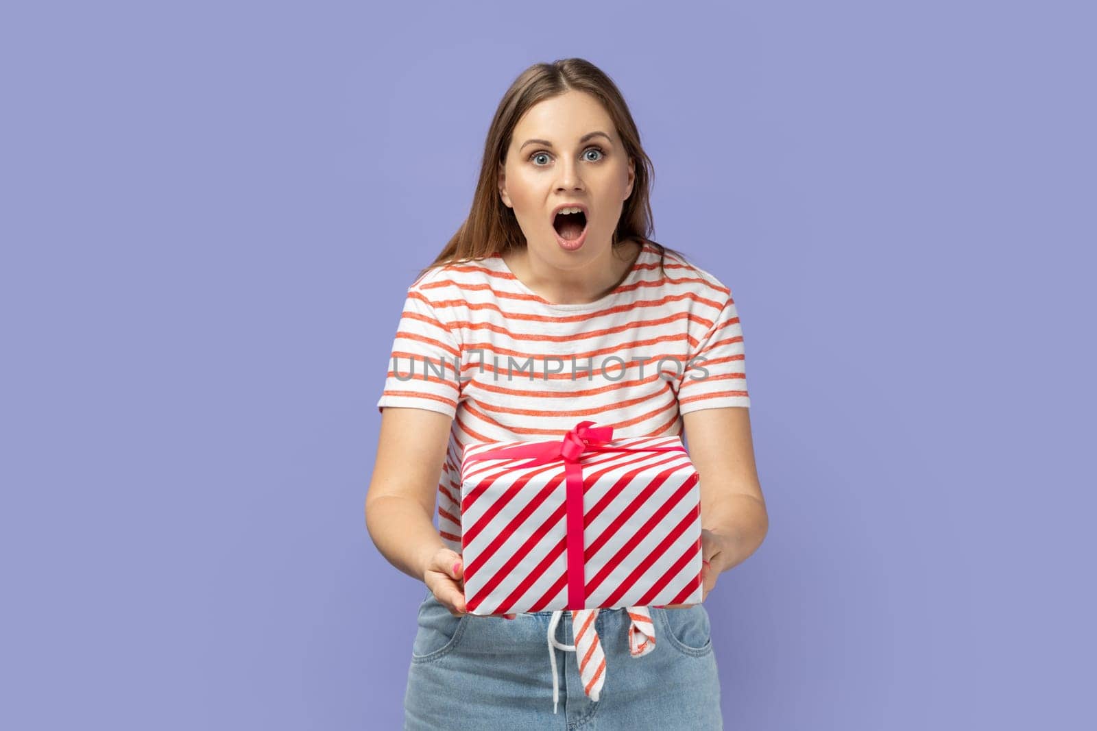 Excited woman giving gift box with amazed facial expression, looking at camera with big eyes. by Khosro1