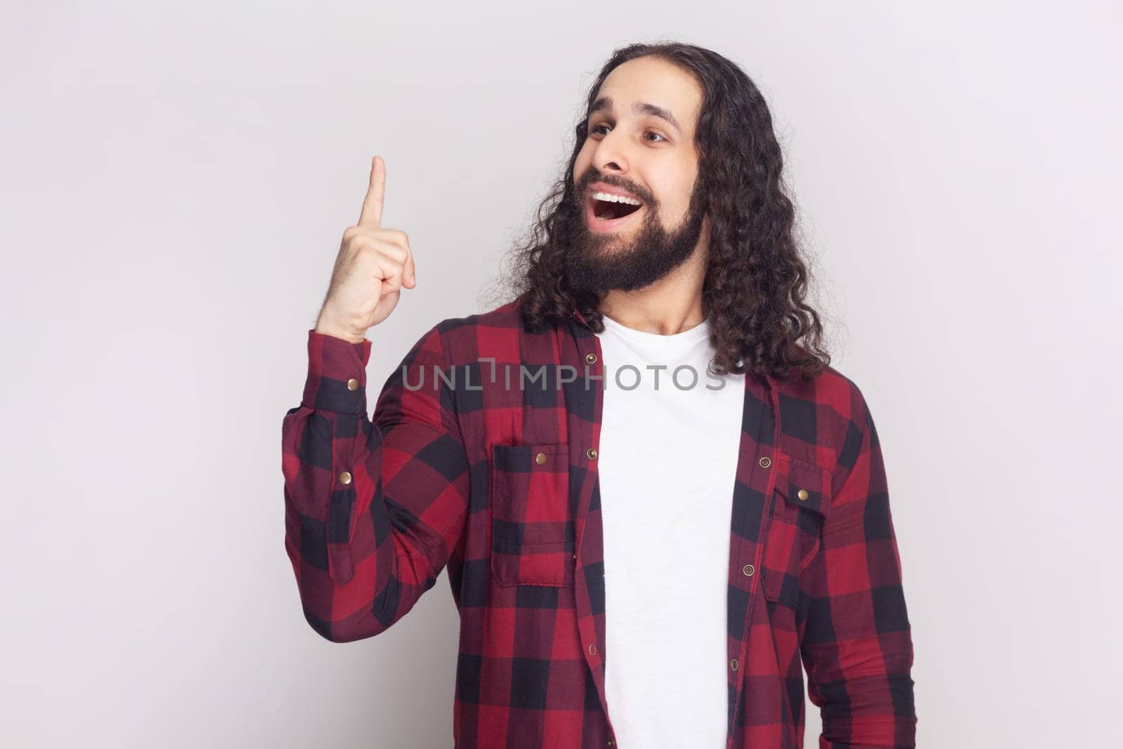 Amazed man with long hair in checkered red shirt raises fore finger as gets some brilliant idea. by Khosro1