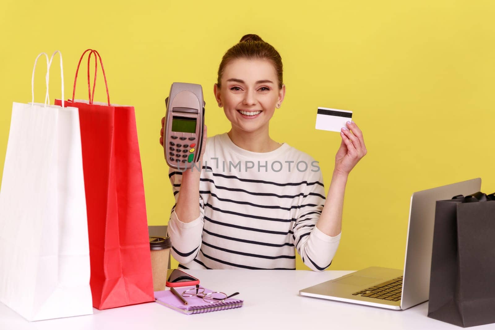 Woman employee sitting at workplace with shopping bags, showing terminal and credit card to camera. by Khosro1