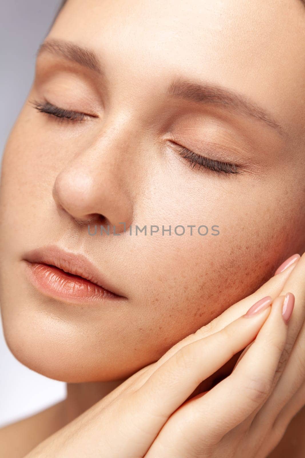 Closeup portrait of calm relaxed beautiful woman posing with closed eyes, girl with natural makeup and manicure. Indoor studio shot isolated over gray background.