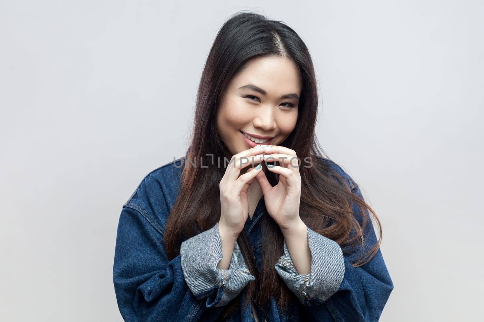 Portrait of mysterious brunette woman in blue denim jacket has interesting plan in mind, intention doing something, everything goes according scheme. Indoor studio shot isolated on gray background.