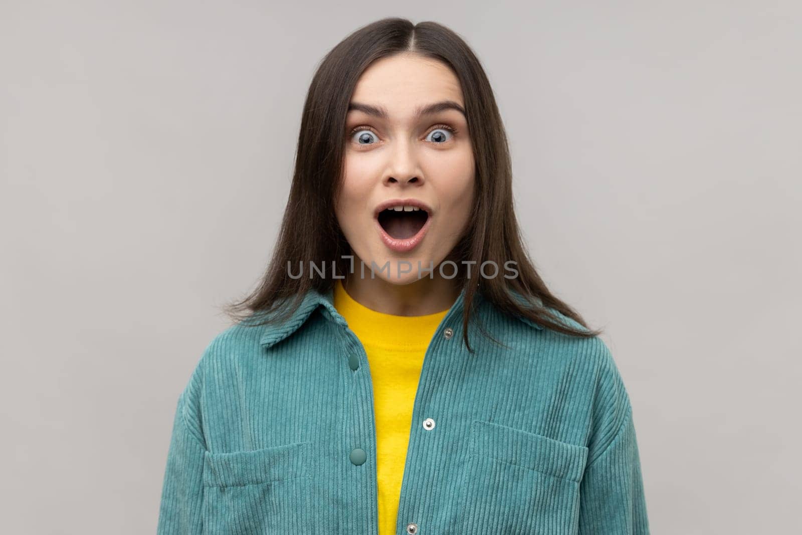 Portrait of astonished woman with widely open mouth in amazement and big eyes looking at camera, stunned shocked face, wearing casual style jacket. Indoor studio shot isolated on gray background.
